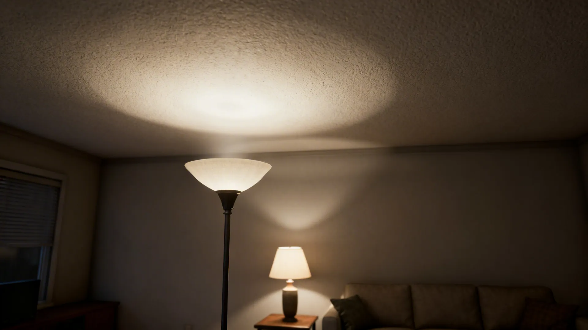 Small living room softly illuminated by an upward-facing torchiere lamp and layered table lighting.