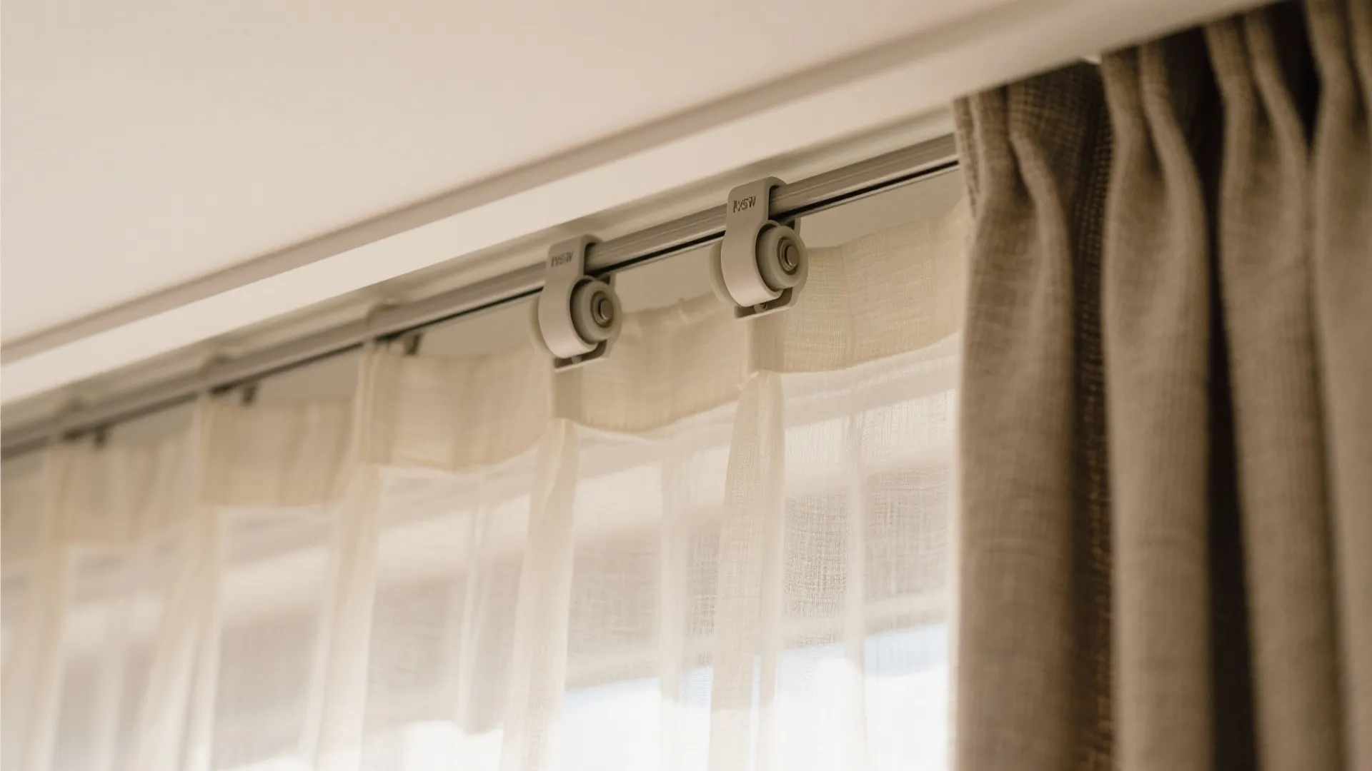 Close up view of white metal curtain track with rollers holding thin white and grey curtains