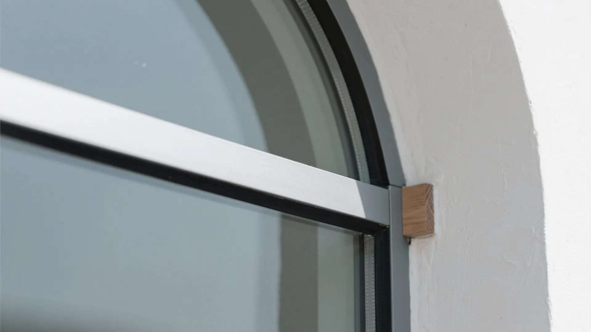 Close up detail of grey arched window frame with wooden joint against white textured plaster wall