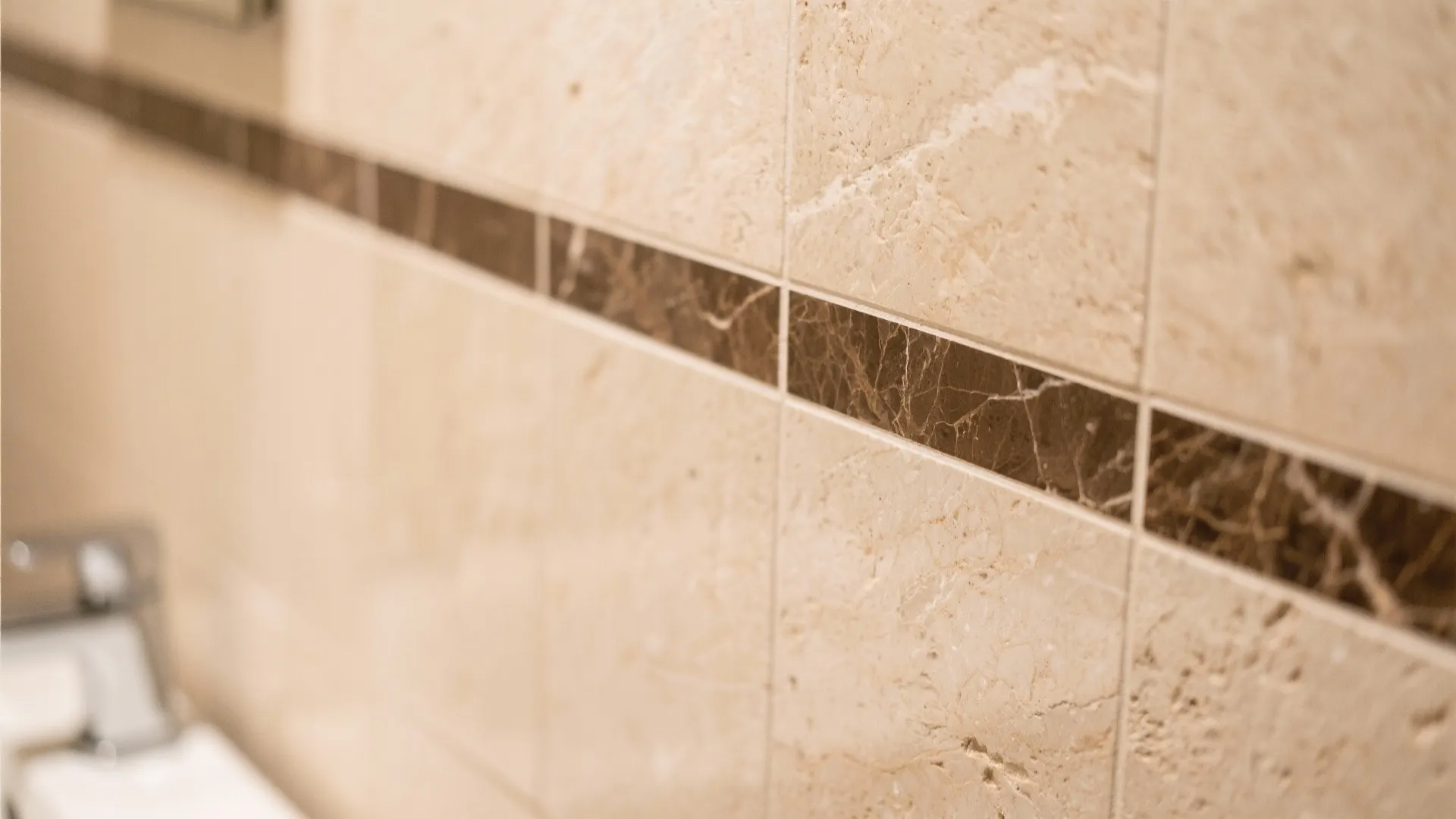 Close up view of light brown stone wall tiles with a dark brown decorative tile border