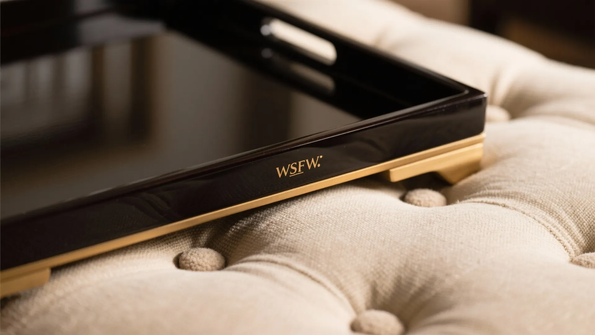 Macro of a lacquer tray edge with felt pads resting on a linen ottoman cushion.