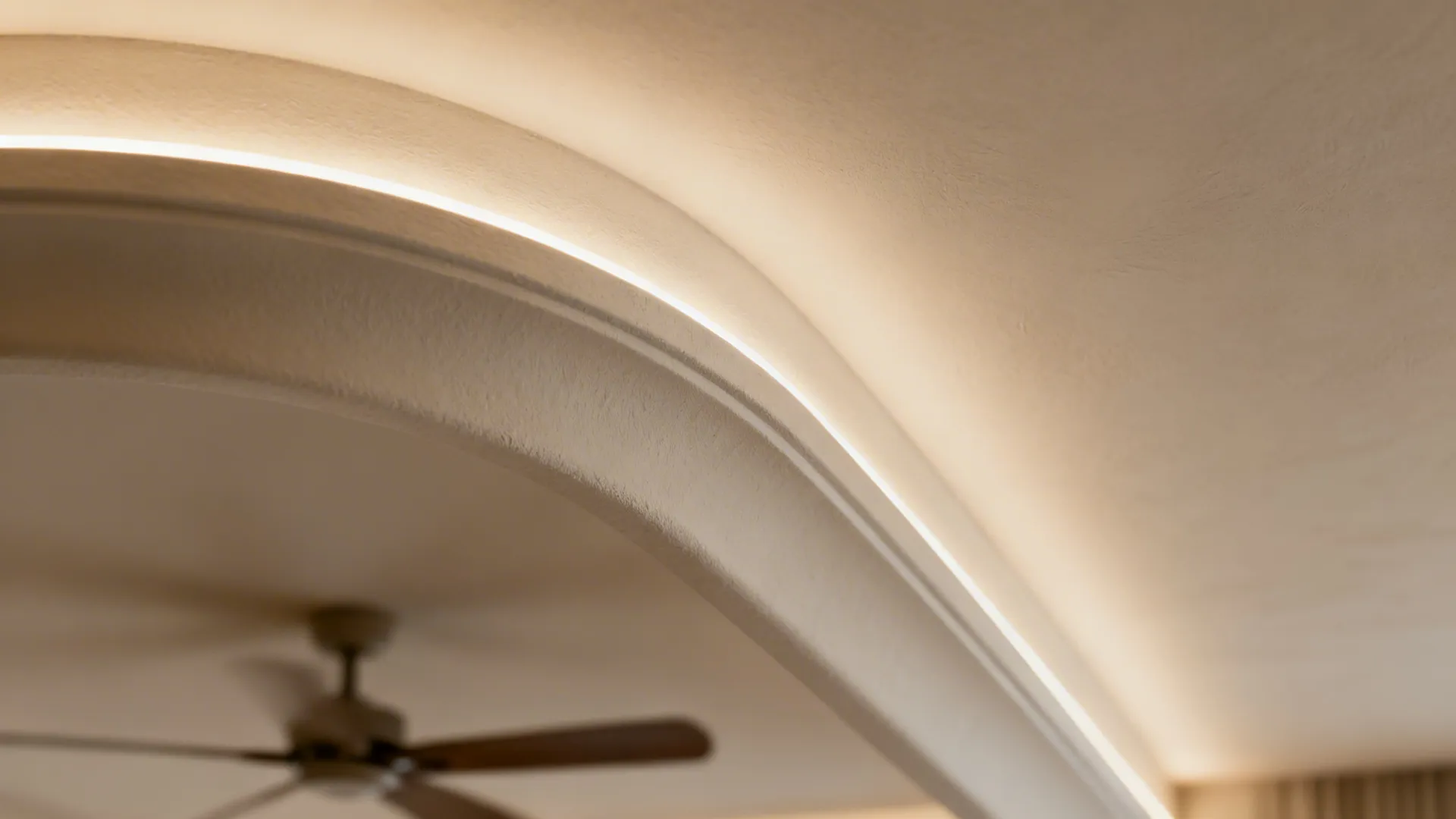 Close-up of a curved tray ceiling lip with warm cove LED wash on smooth plaster.