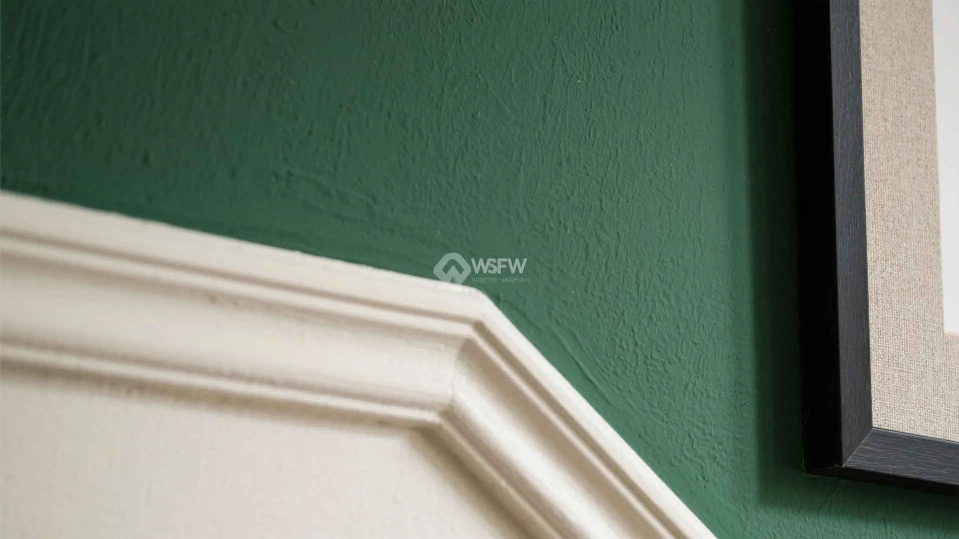 Close up of white wall panel against dark green wall next to black picture frame corner