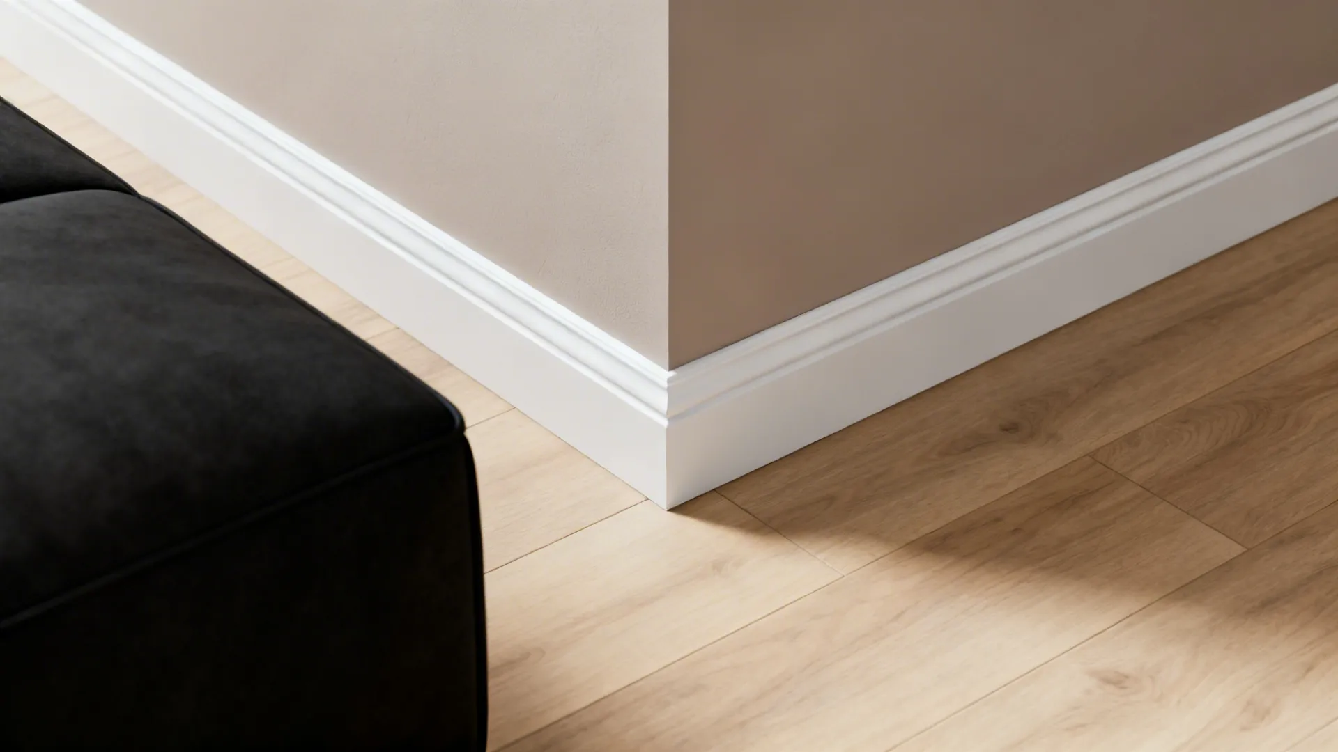 Crisp white trim framing a soft taupe wall and pale oak floor next to a black sofa corner.