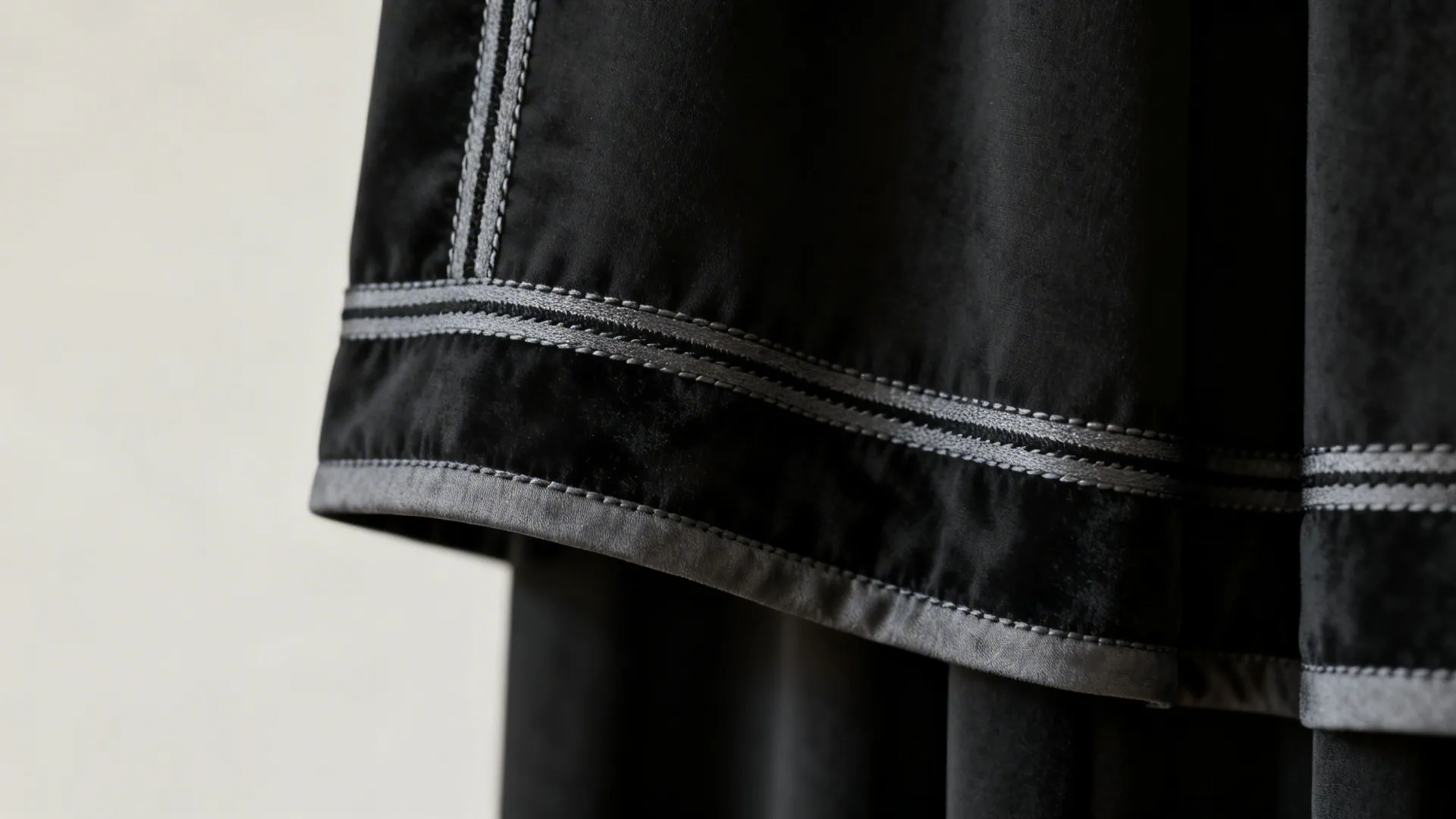 Close up of black curtain fabric showing grey trim details with double stitching on wall