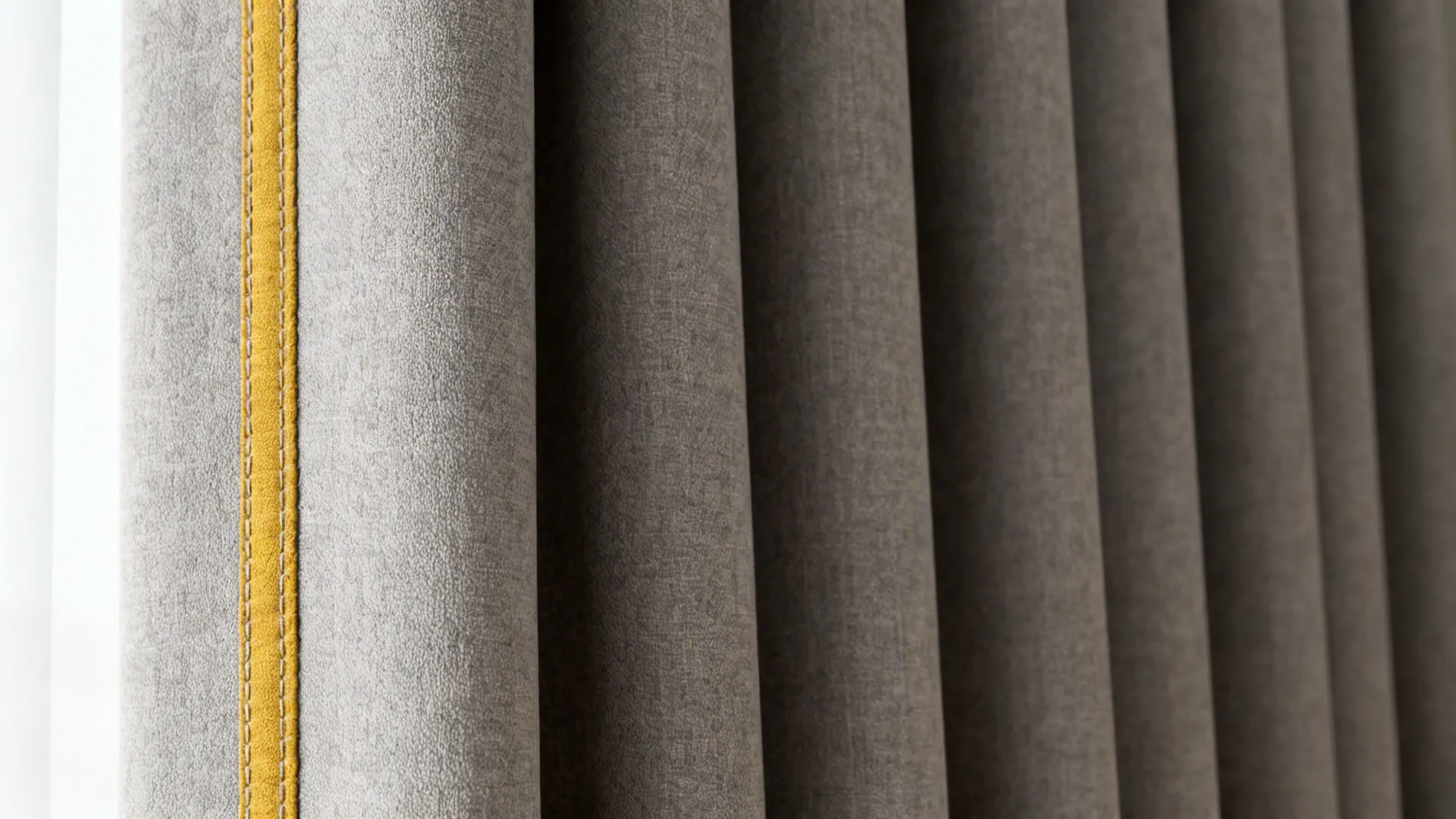 Close-up of grey curtain fabric with neat mustard yellow piping and visible stitch detail.