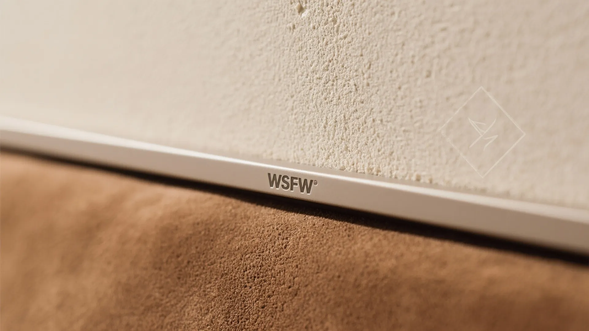 Thin silver metal trim with letters between a cream wall and a brown fabric surface