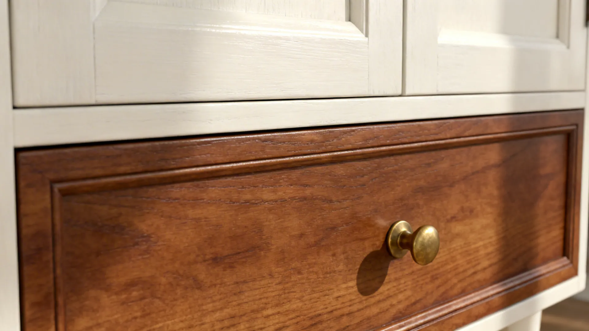 Close-up of warm white upper cabinet meeting walnut drawer with a brass pull.
