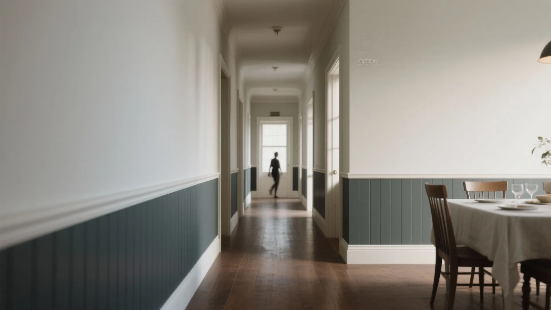 Long hallway featuring white walls with dark grey wall panel wood floor and dining table