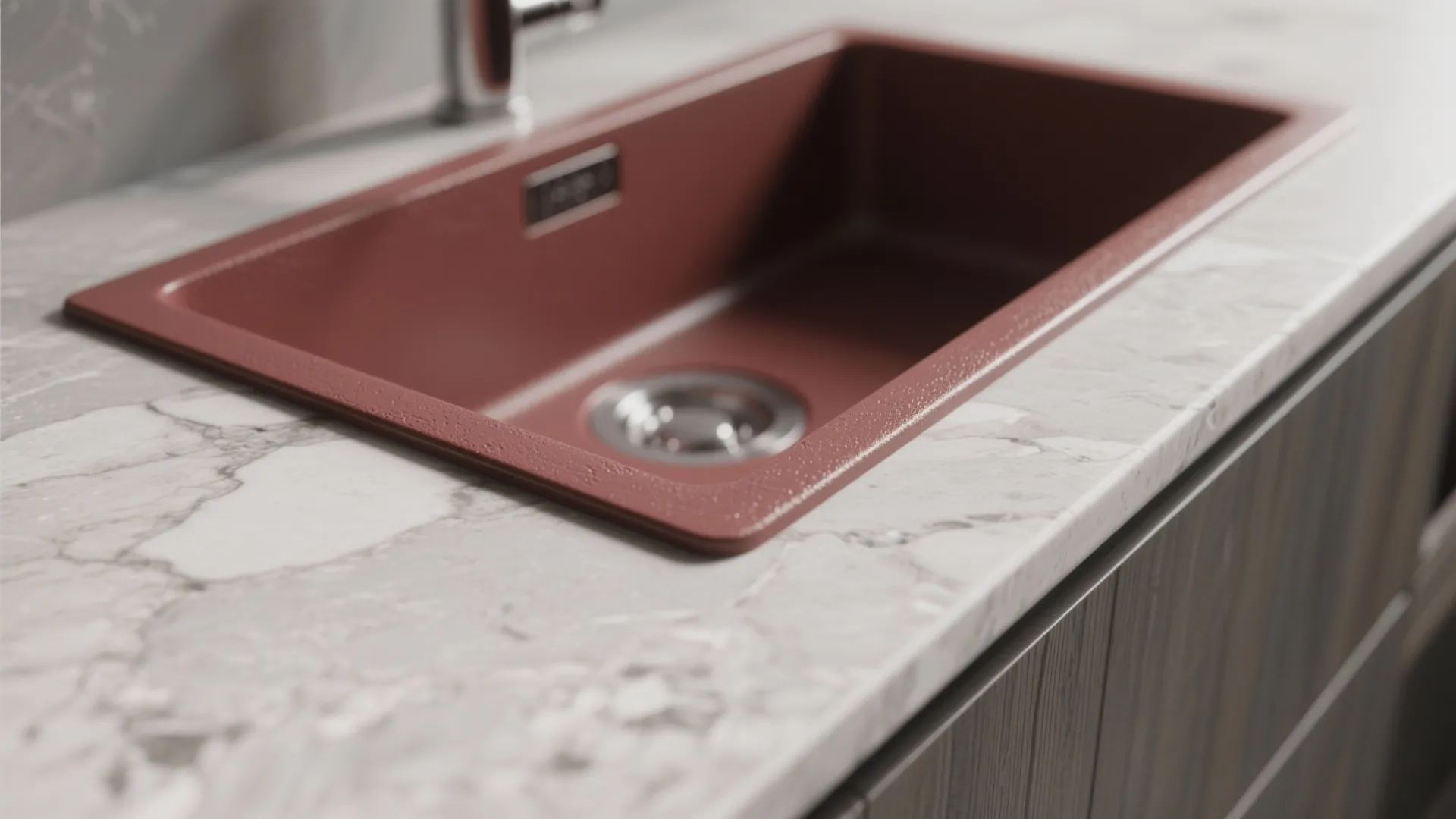Matte red kitchen sink installed in white marble countertop with grey veins and dark wood cabinet