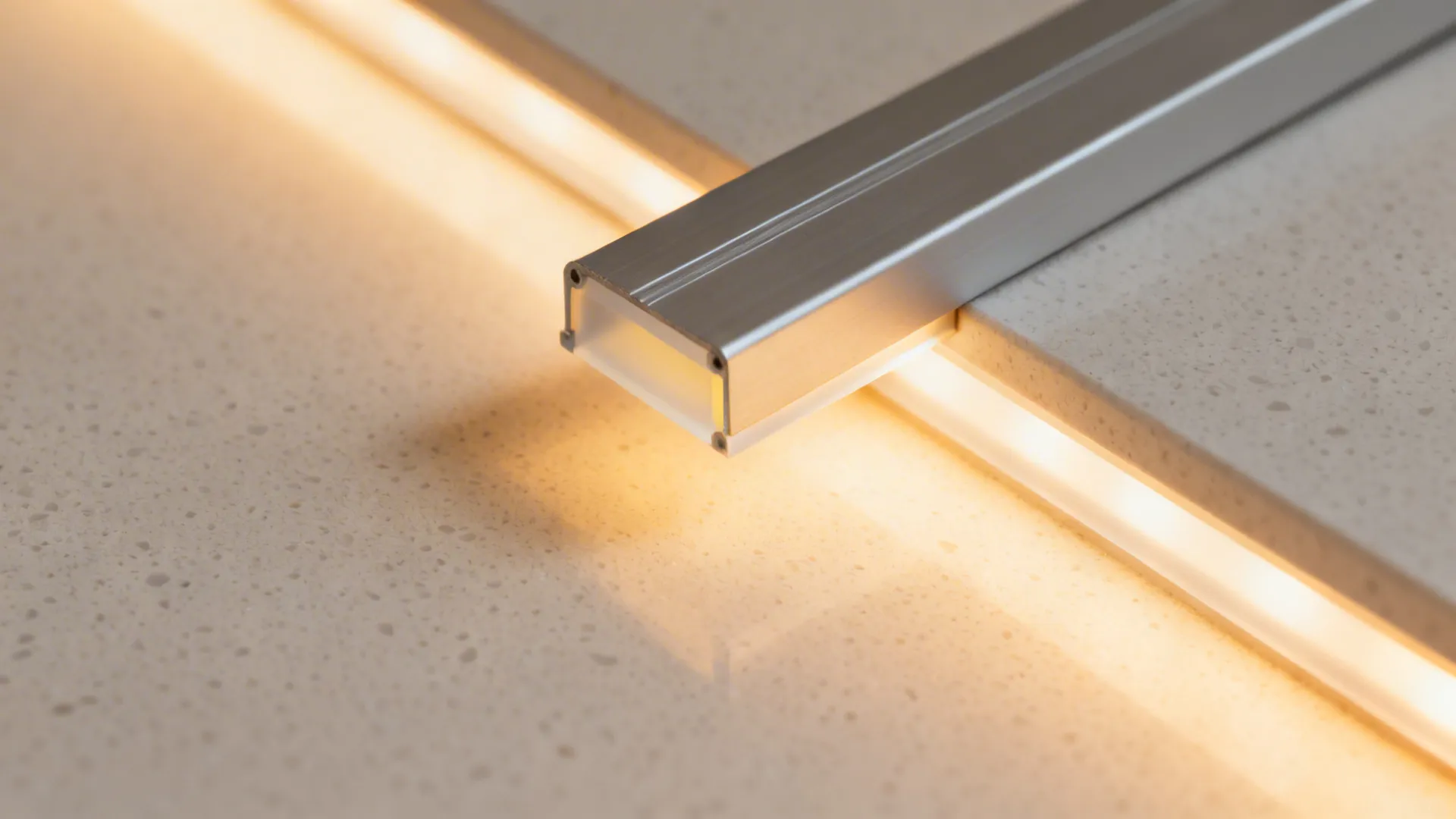Modern aluminum light fixture with warm glow installed on a light colored stone kitchen surface