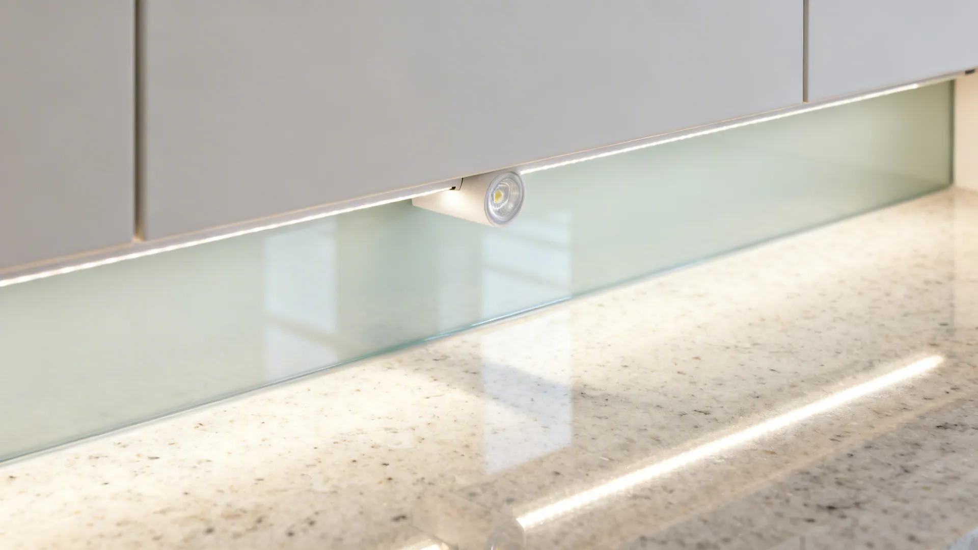 Macro of under-cabinet LED strip evenly lighting a quartz counter and satin glass backsplash.