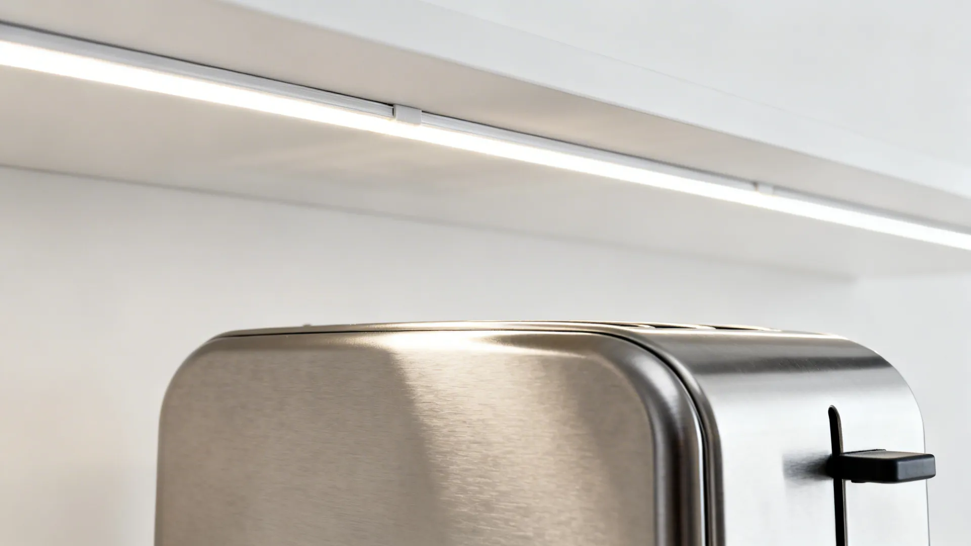 Stainless steel toaster sitting under a white shelf with a bright light fixture turned on