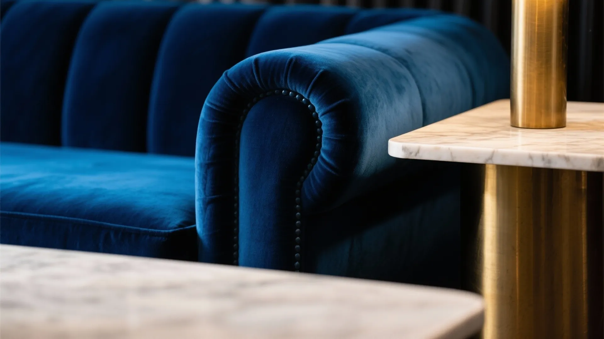 Close up of a blue velvet sofa next to a marble side table with gold base