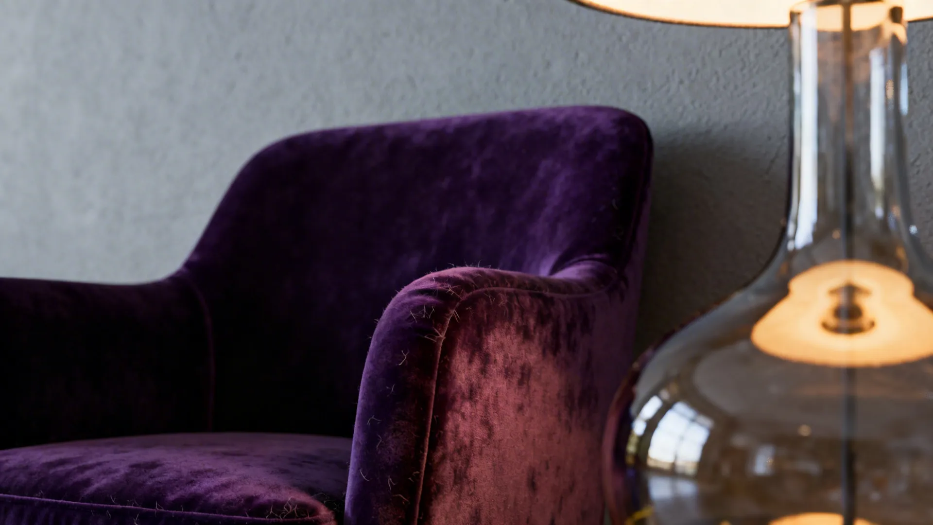 Close up of a purple velvet armchair placed next to a modern glass table light fixture