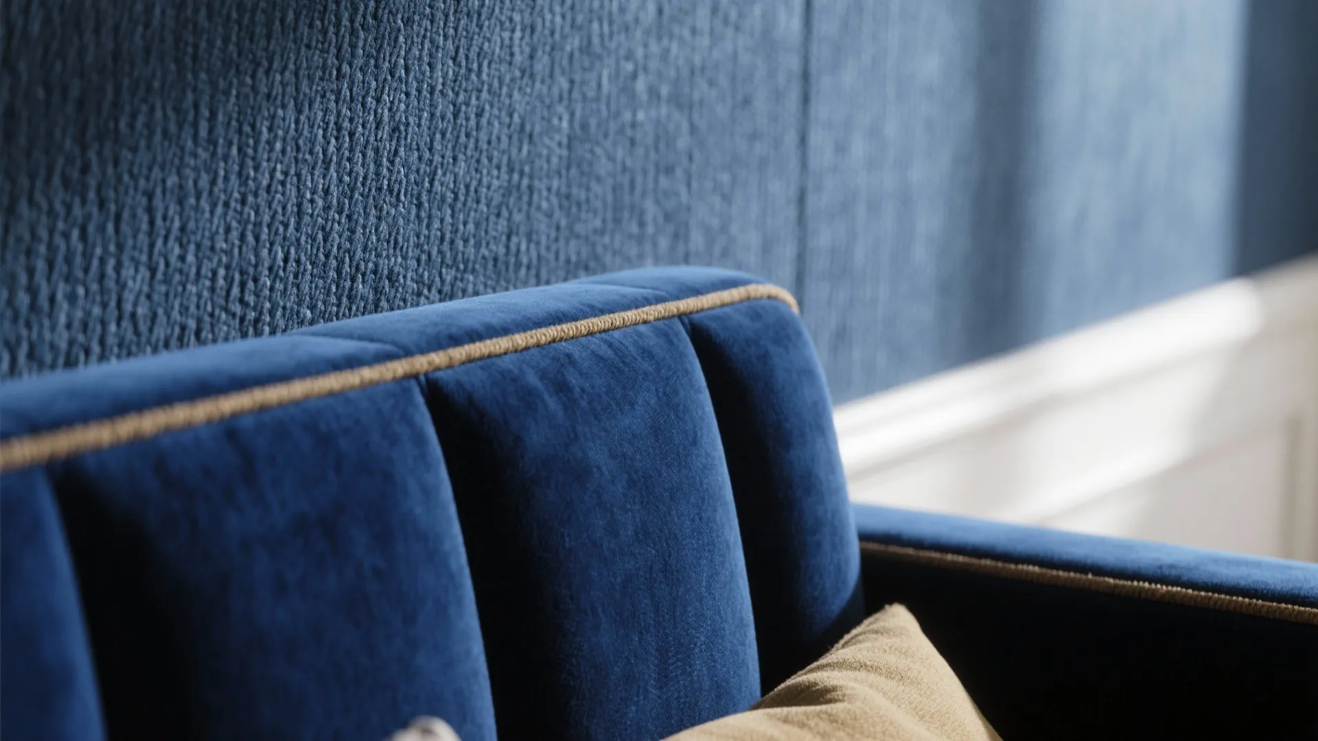 Close up of blue velvet sofa with gold piping and textured blue wall with soft light