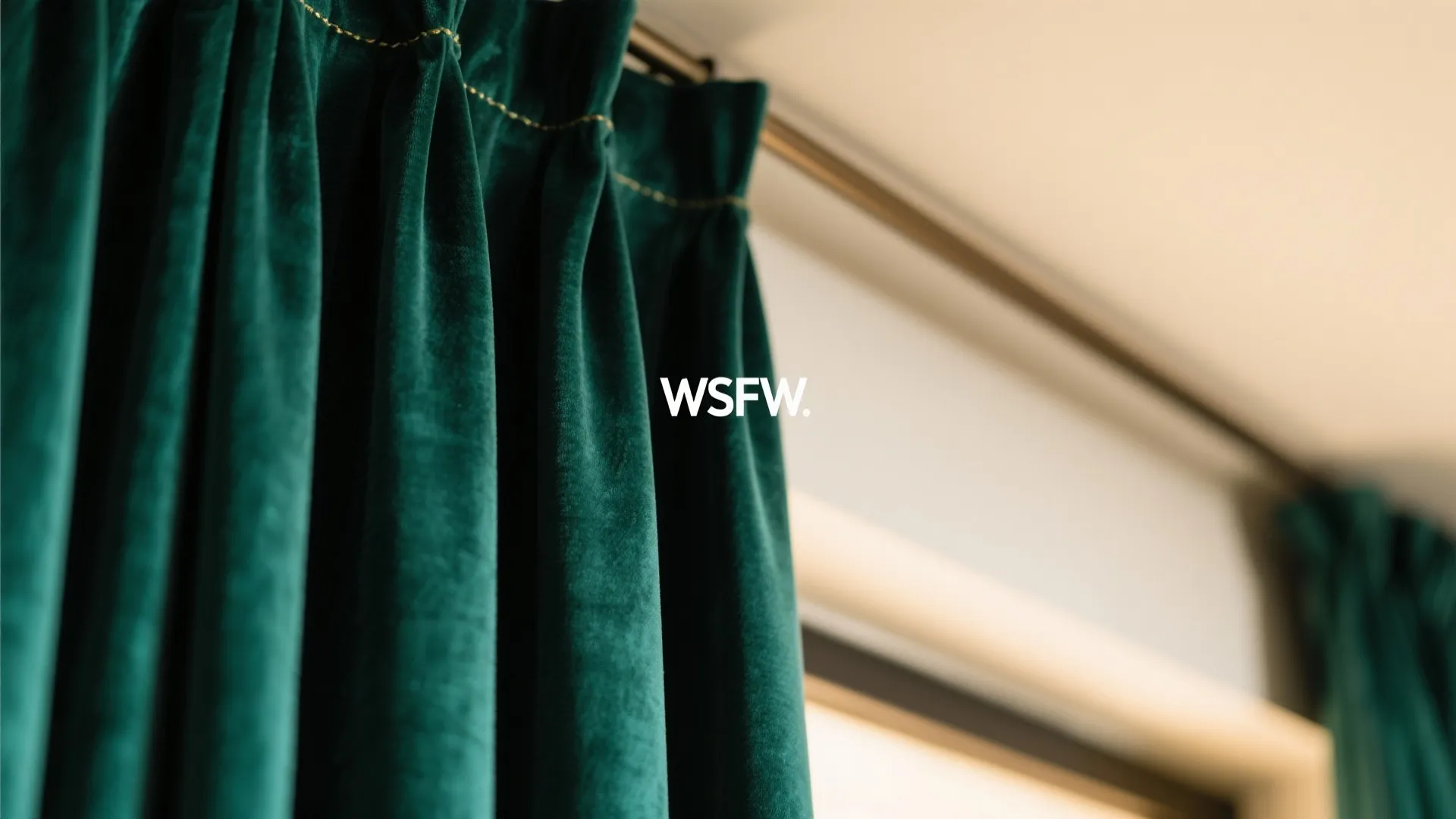 Close-up of green velvet curtain hanging on a metal track with gold stitching for window