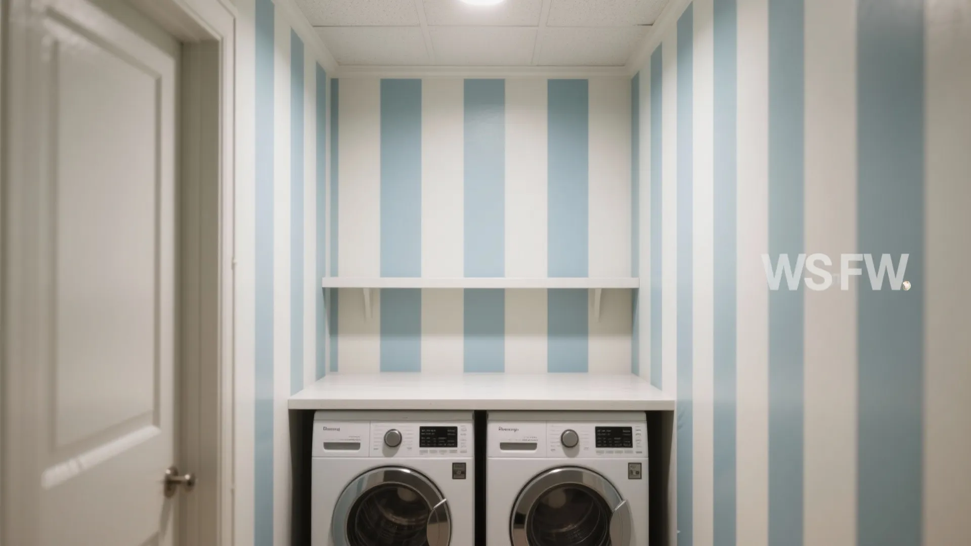 Laundry room featuring blue vertical striped wallpaper two washing machines and one white wall shelf