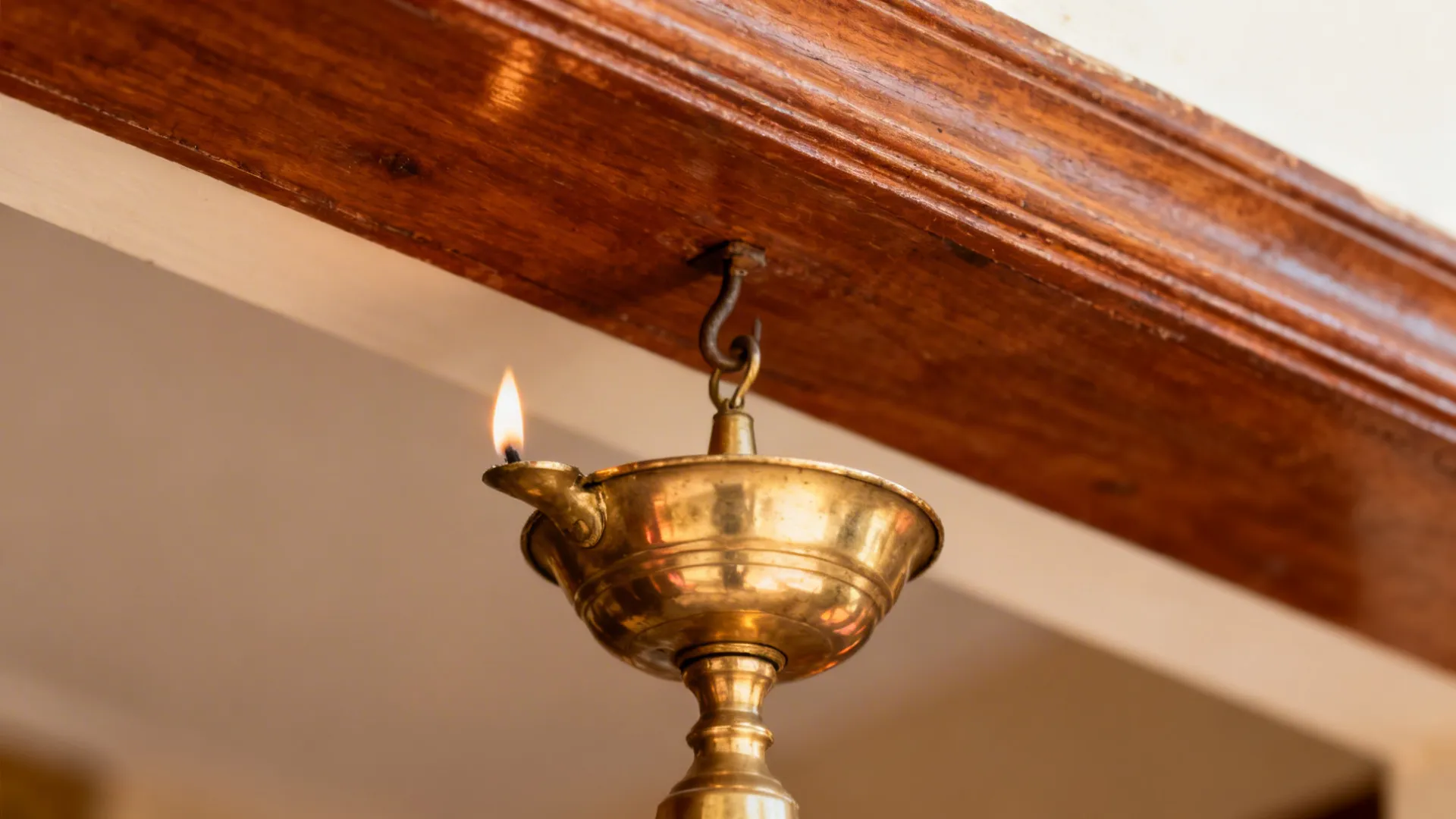 Close-up of a brass vilakku hanging under a wooden temple-style cornice.