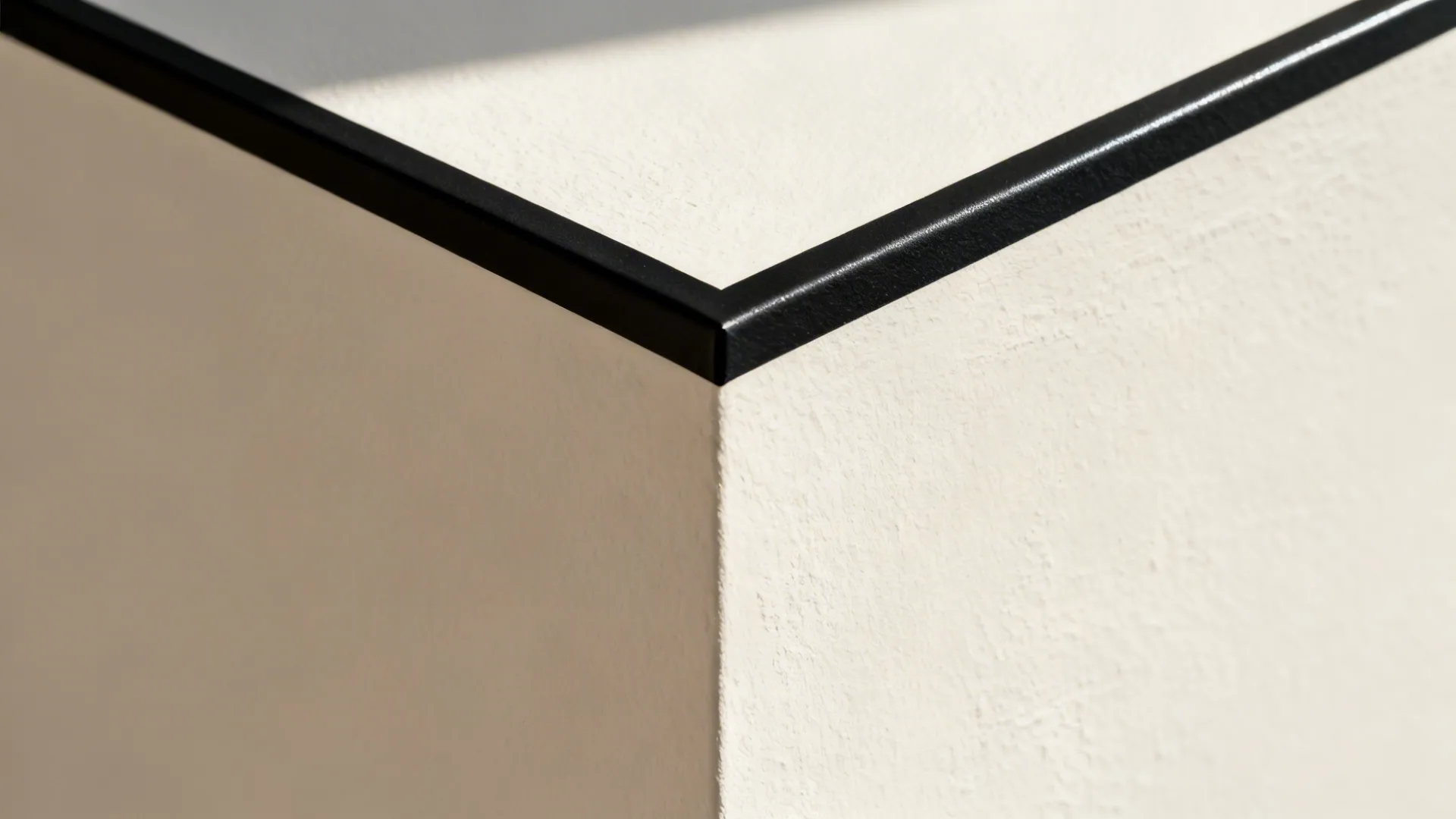 Macro of a matte black vinyl decal edge on a smooth eggshell wall with soft daylight.