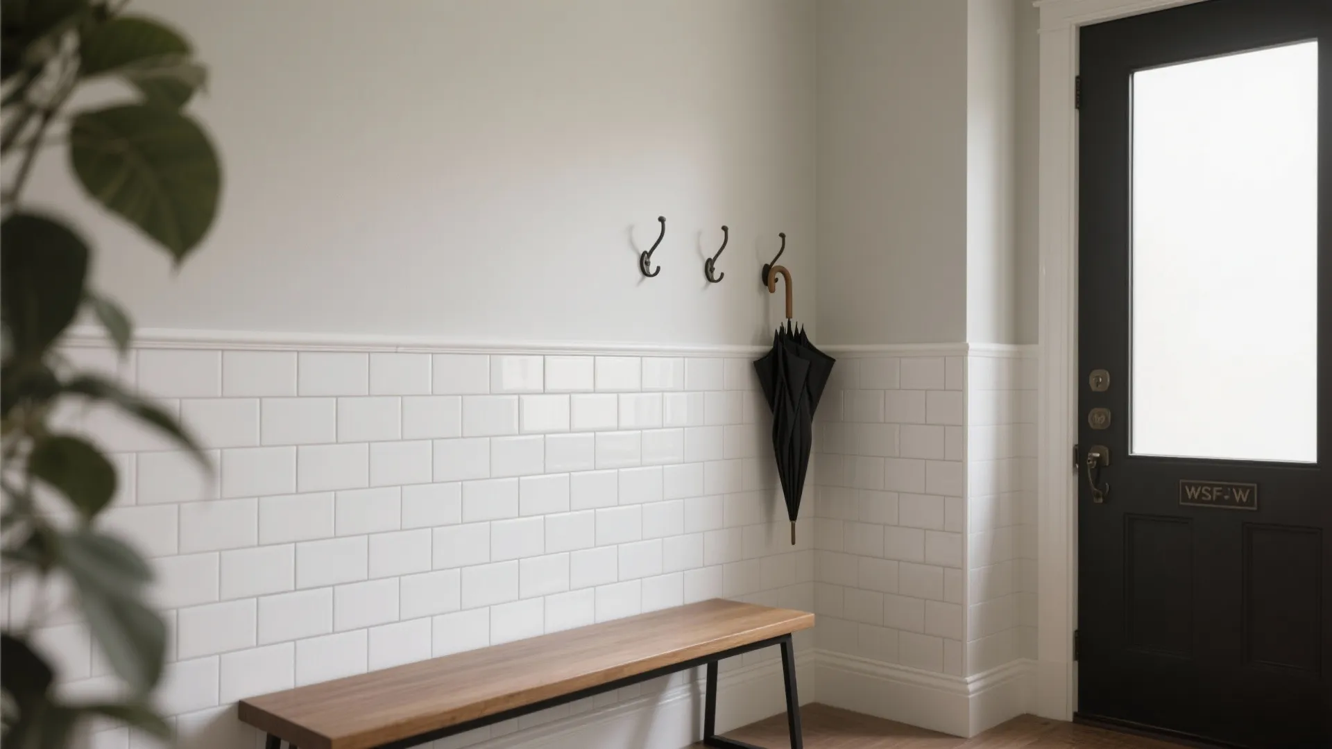 Entryway with white wall panel, wooden bench, black umbrella on hooks, and a black door