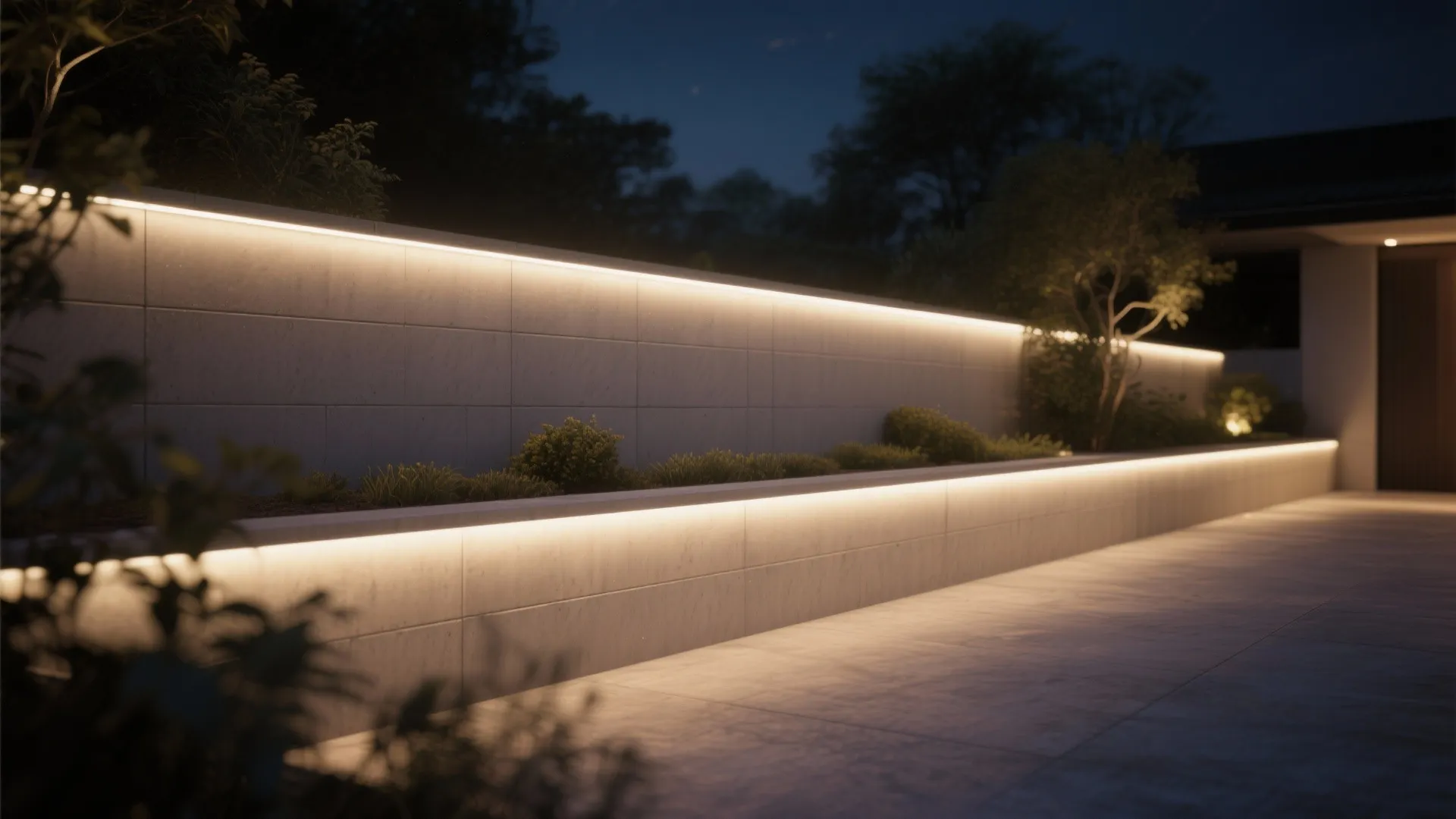 Modern outdoor garden wall with warm LED strip light at night beside a paved path