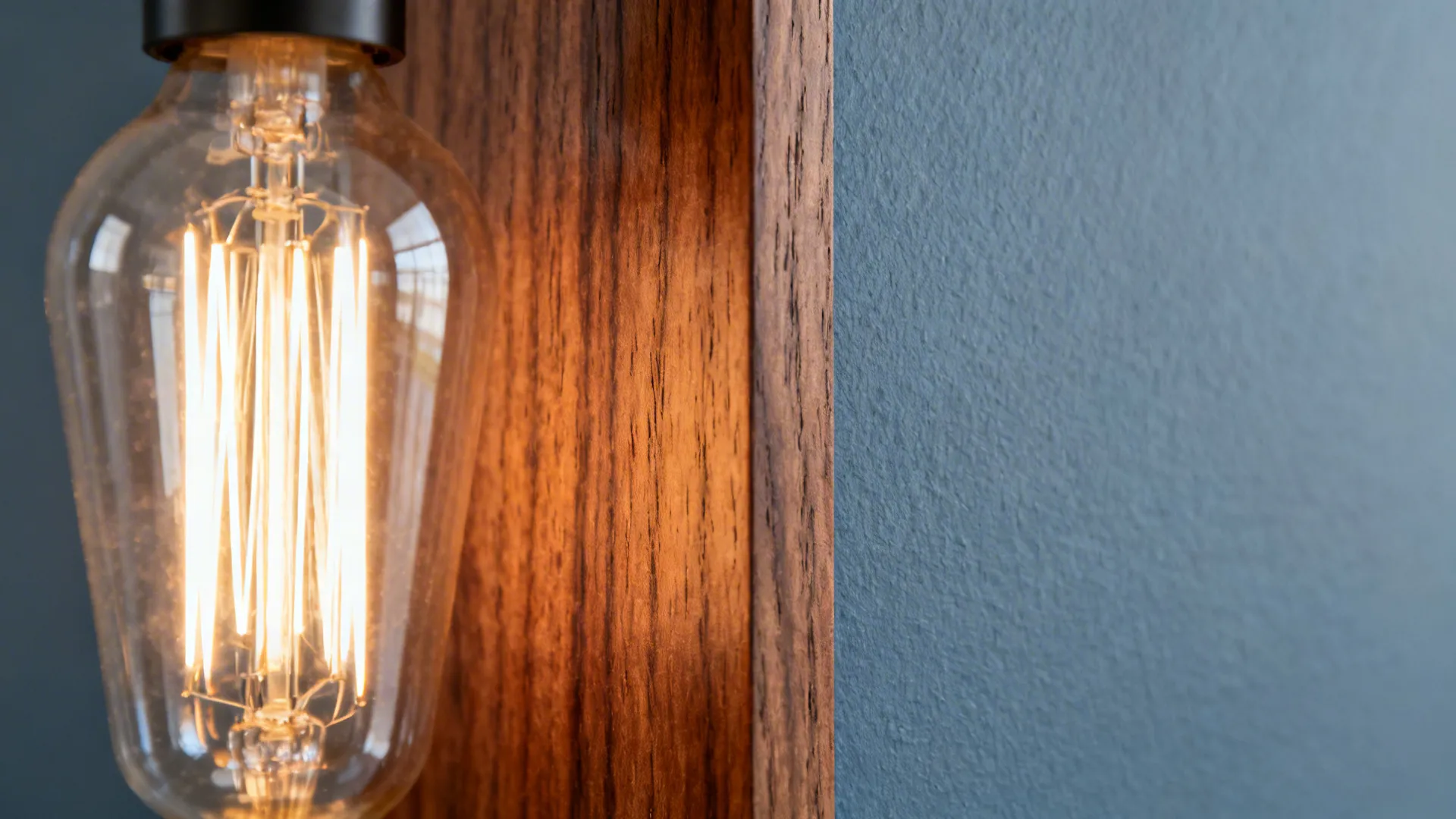Macro of walnut grain beside a blue-gray wall showing satin finish and subtle texture.