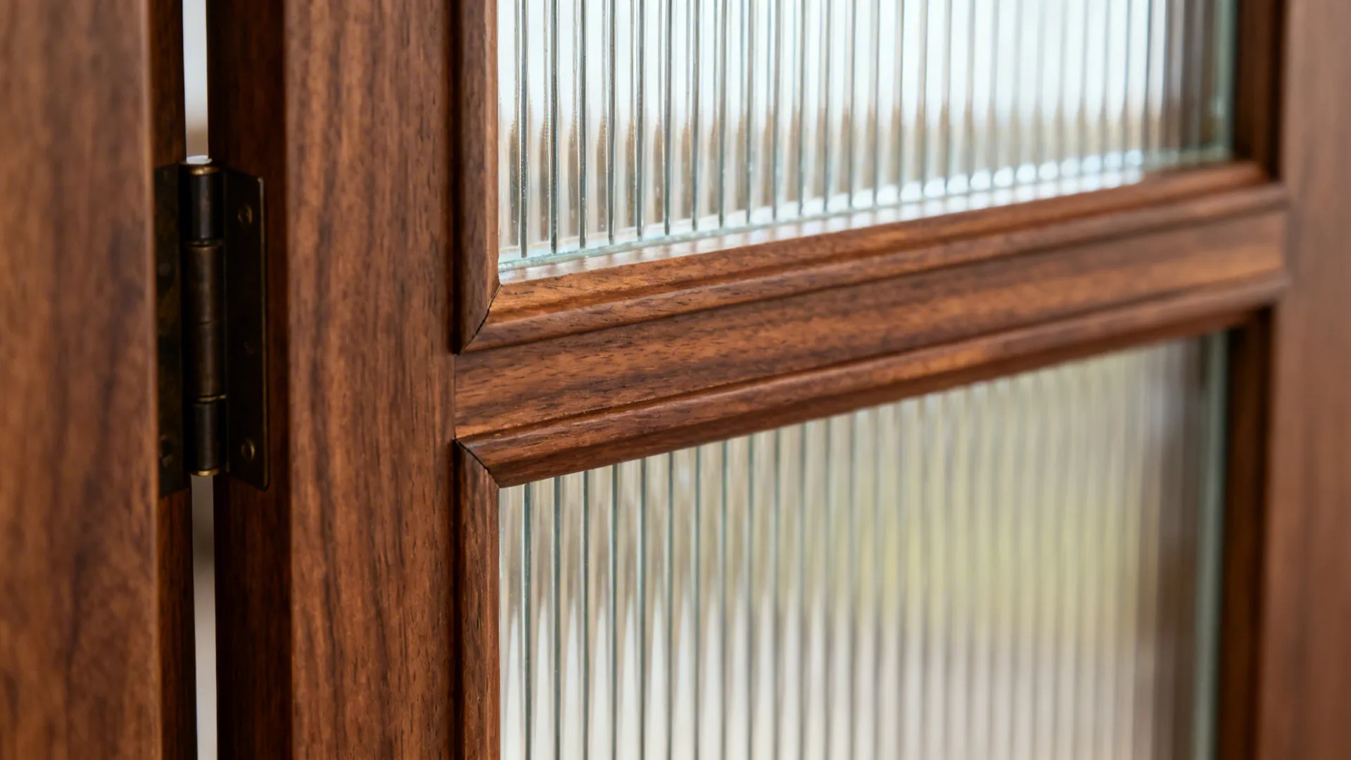 Close up of a dark wood cabinet door with ribbed glass panels and metal hinge