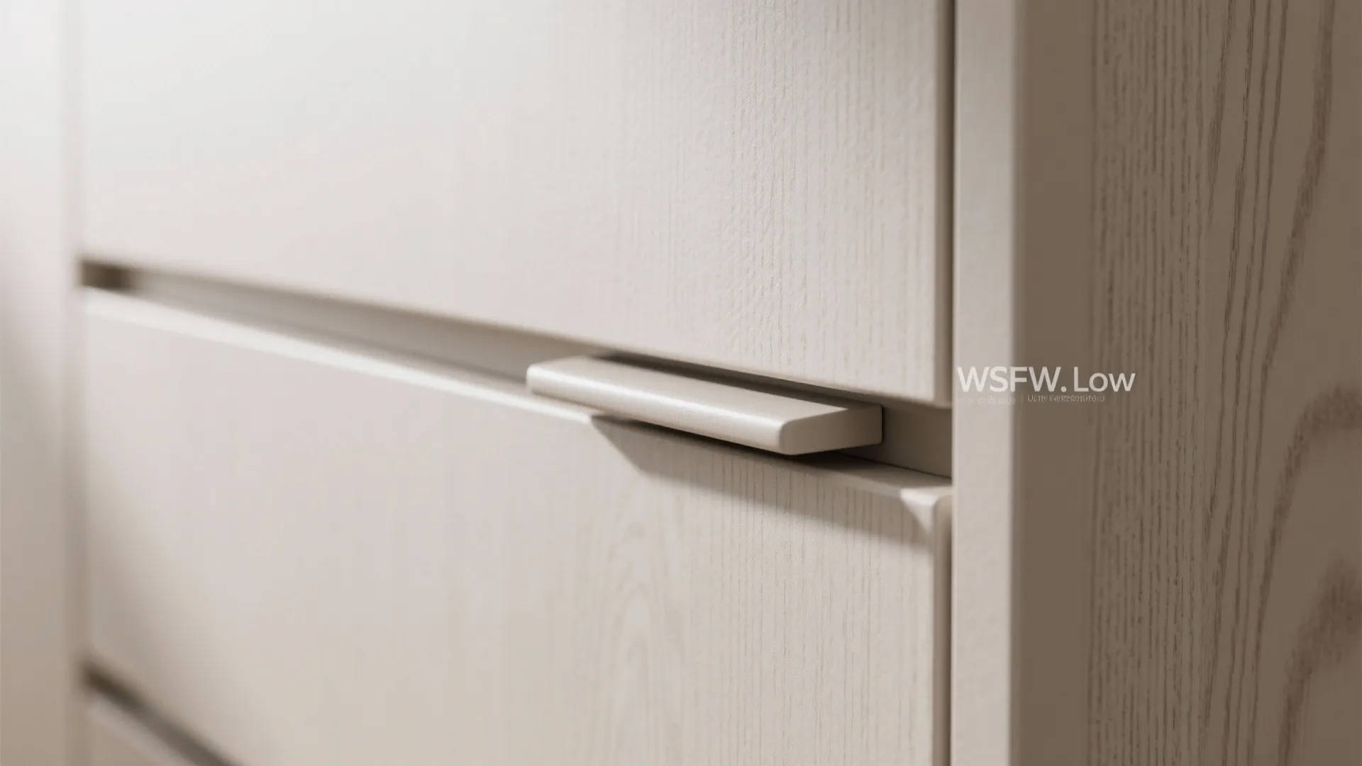 Close up of a cream wooden cabinet drawer with a slim metal handle and wood grain