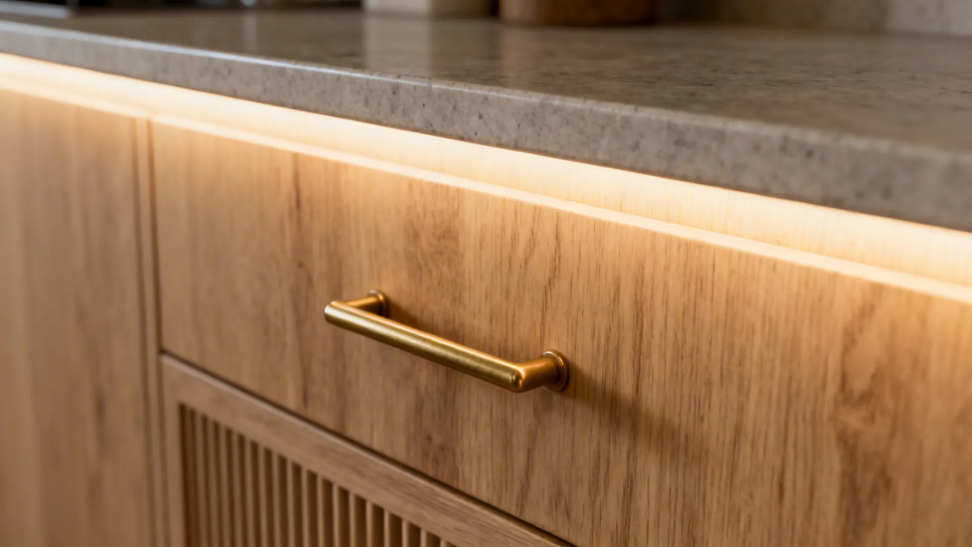 Macro of light oak cabinet with brushed brass pull and matte stone counter under warm LED glow.