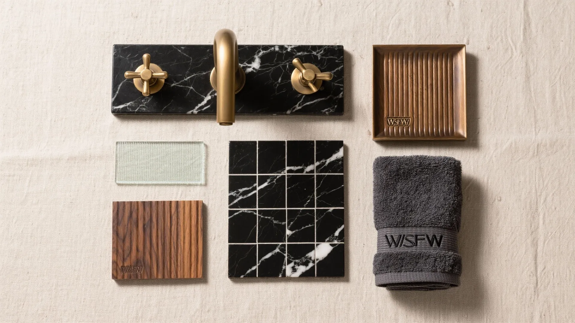 Flat lay of brass and bronze hardware, fluted oak, ribbed glass, charcoal textiles, and honed black marble tiles for a warm balanced palette.
