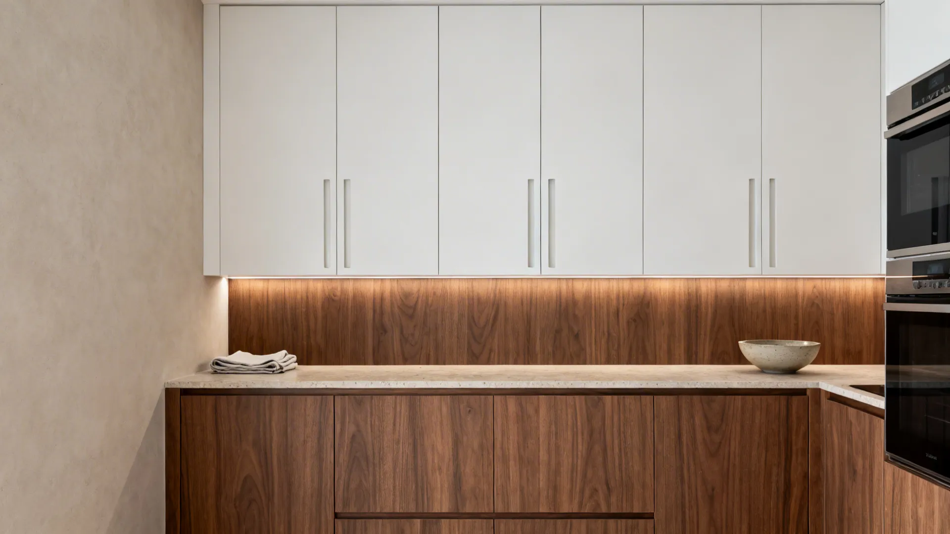 White kitchen cabinets with under cabinet lighting, wood wall panel, marble countertop, and black ovens