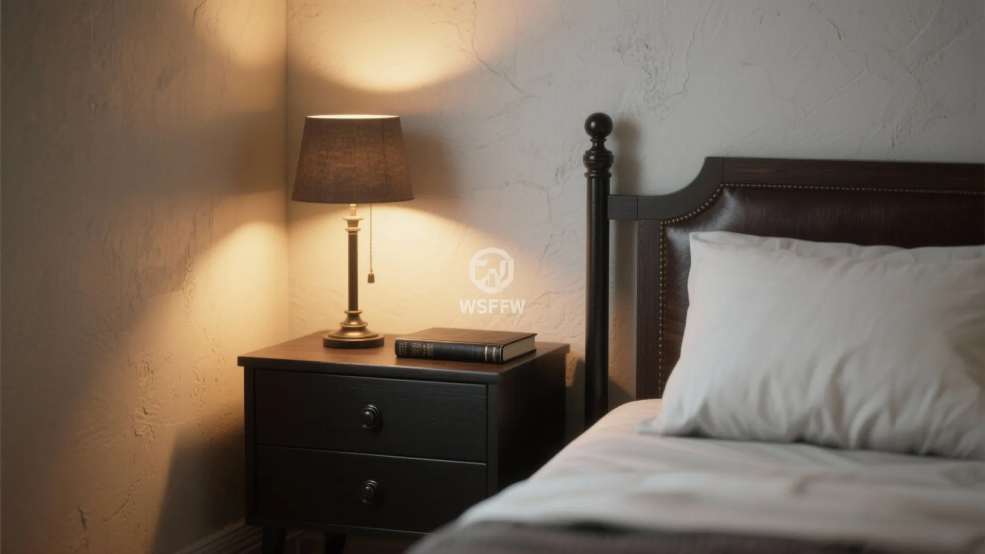A black bedside table with a table light and book next to a wooden bed