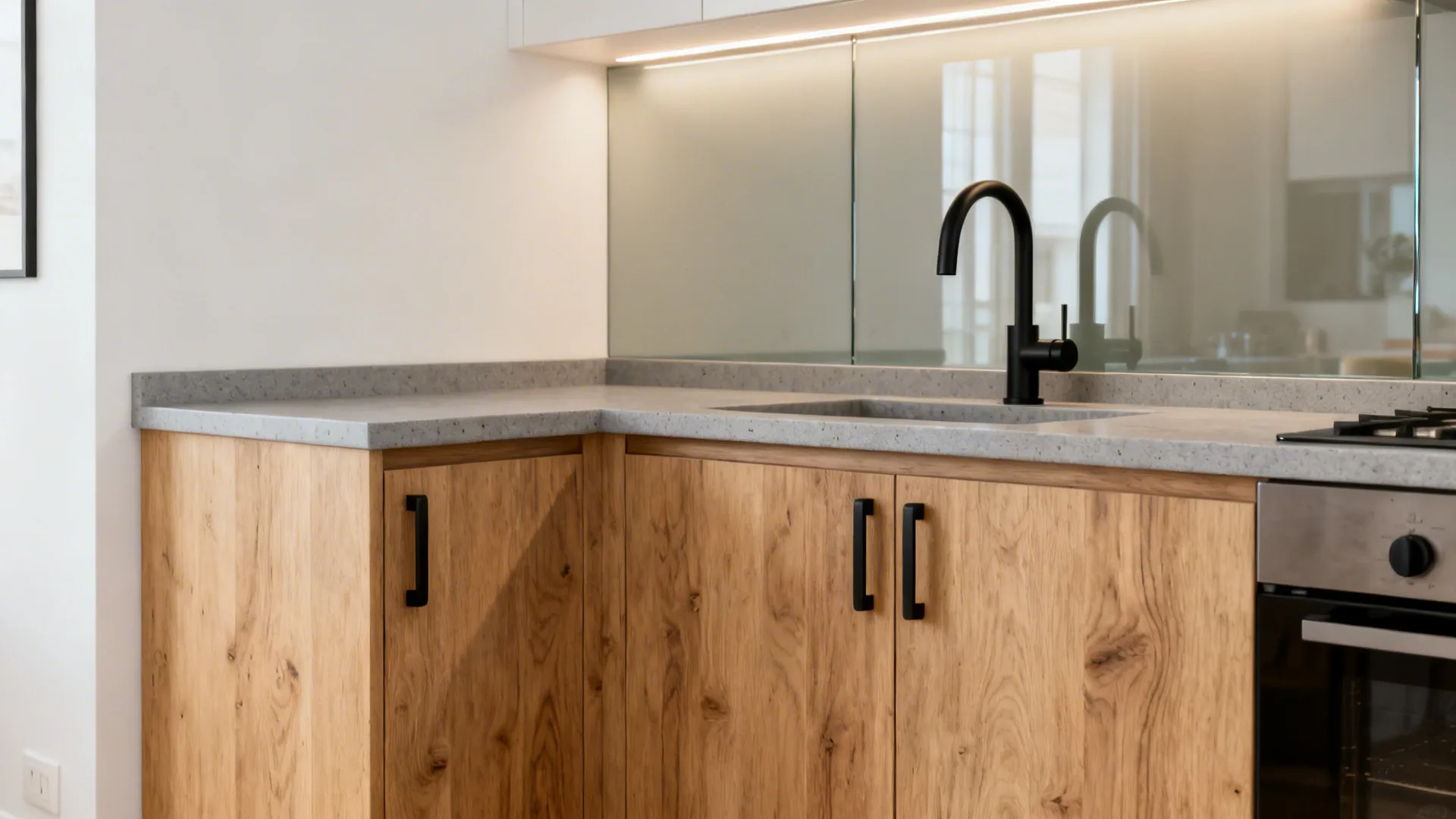 Light oak cabinets with matte black hardware and pale gray quartz in a calm modern kitchen.
