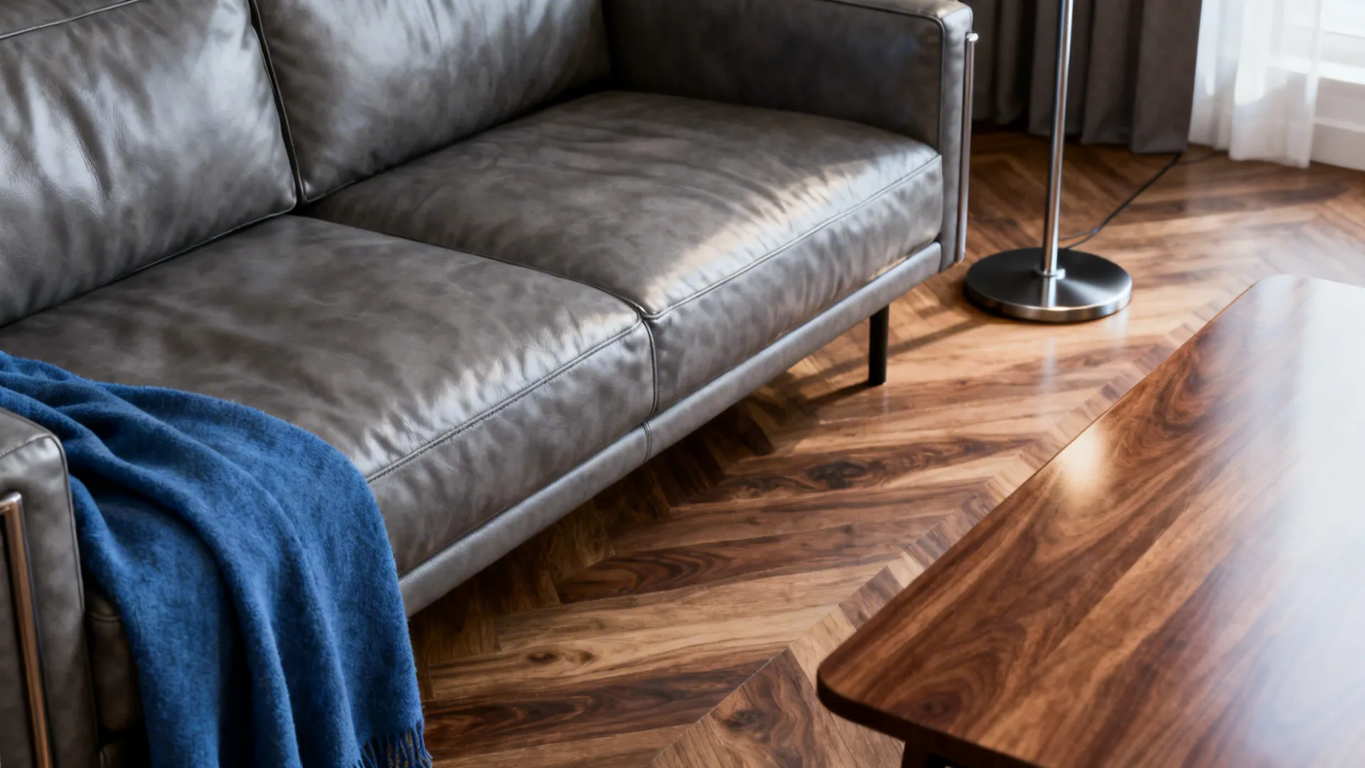 Modern grey leather sofa with blue blanket on wood floor near a wooden coffee table