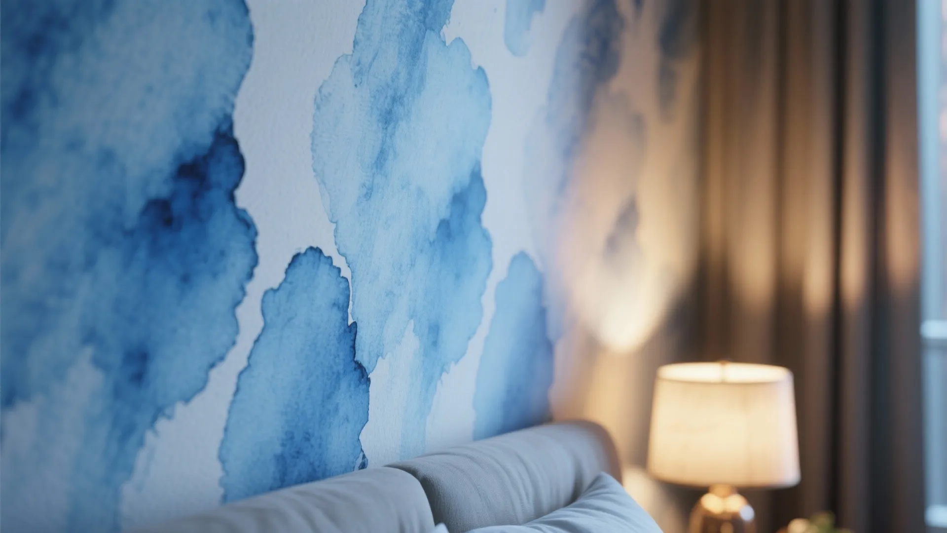 Close up view of blue watercolor wall design next to a bed and warm lamp