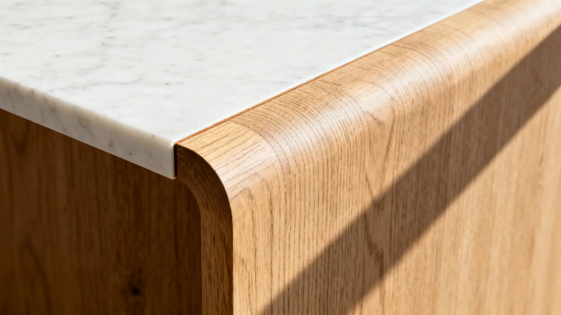 Detail of white marble countertop meeting a curved light wood panel on modern kitchen island