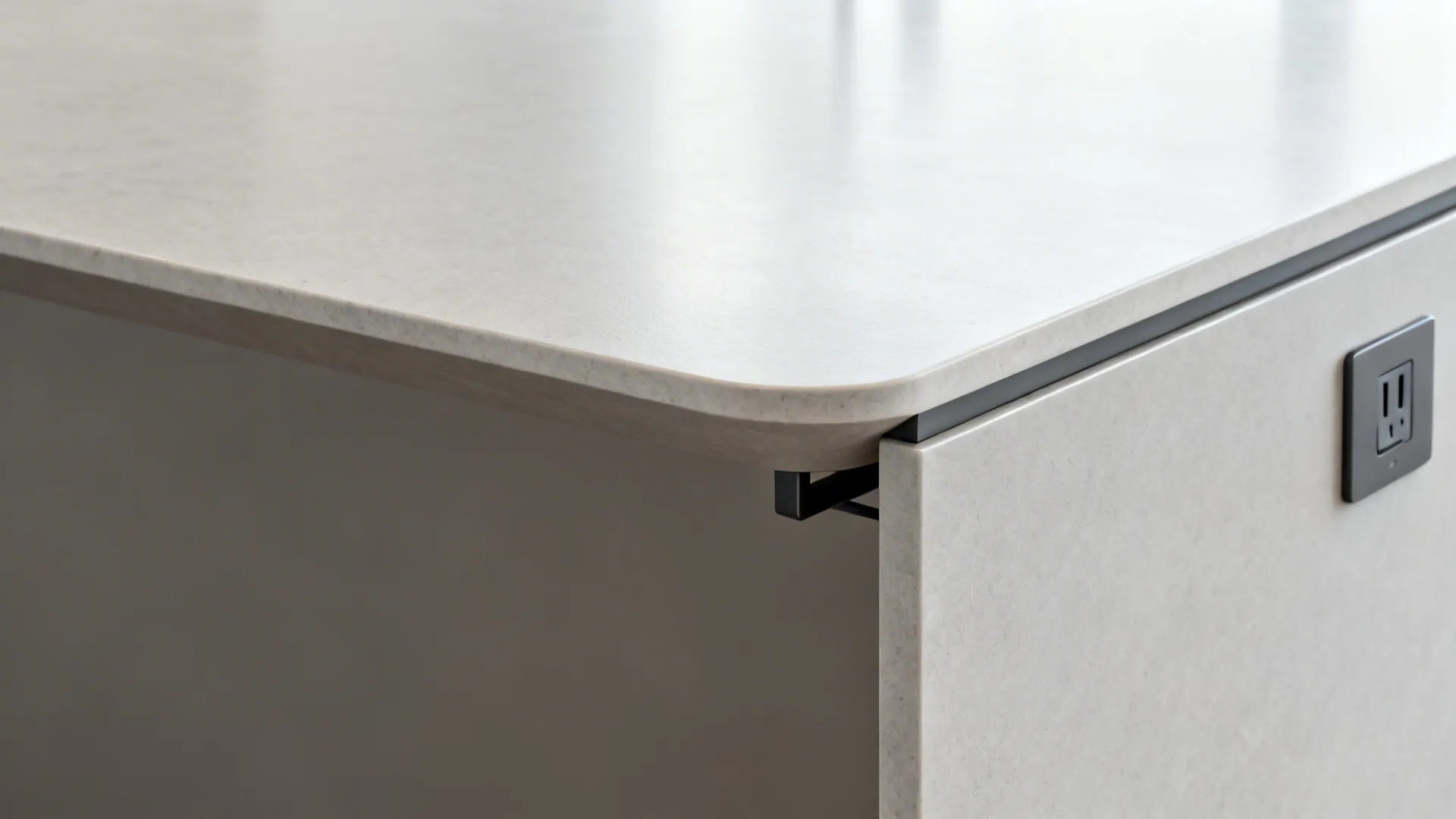 Close up of white stone countertop edge with a black power outlet built into side