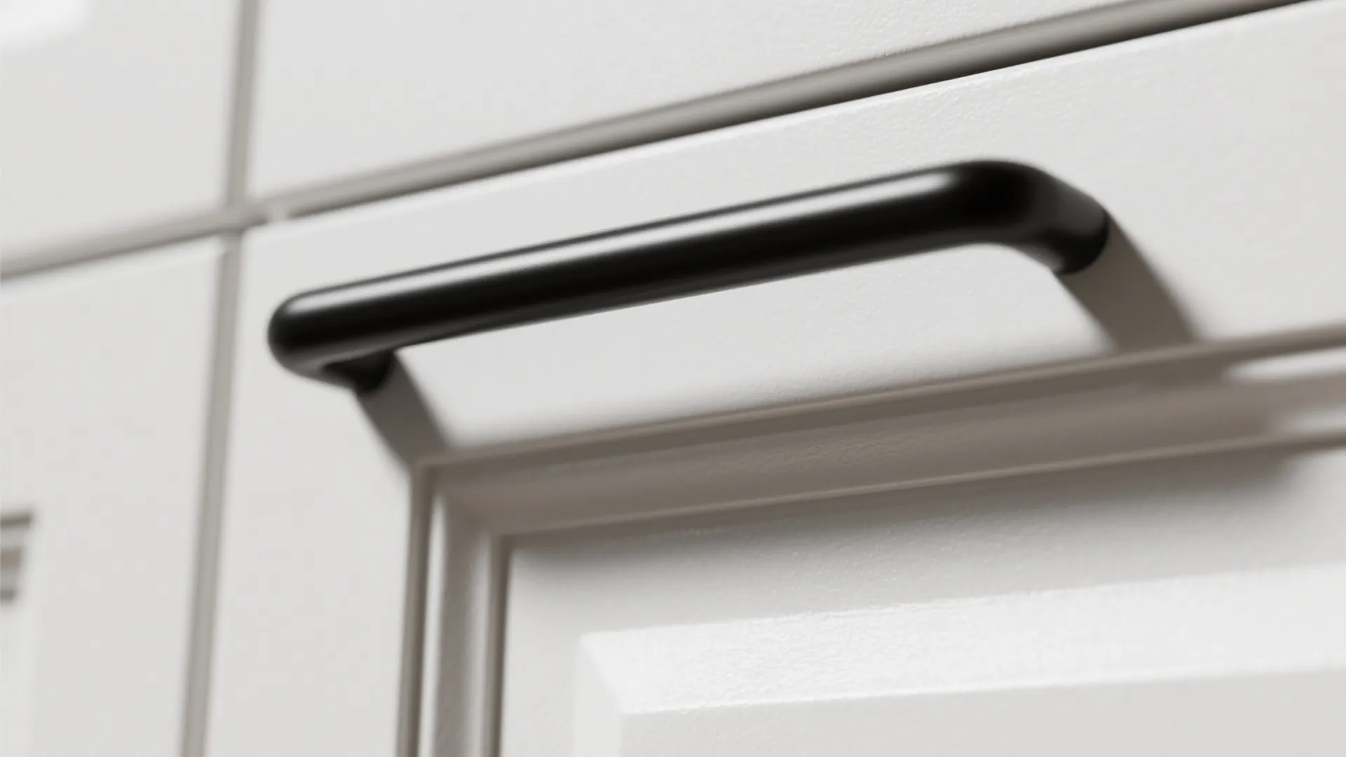 Close-up of a matte black bar handle on a white semi-matte cabinet door
