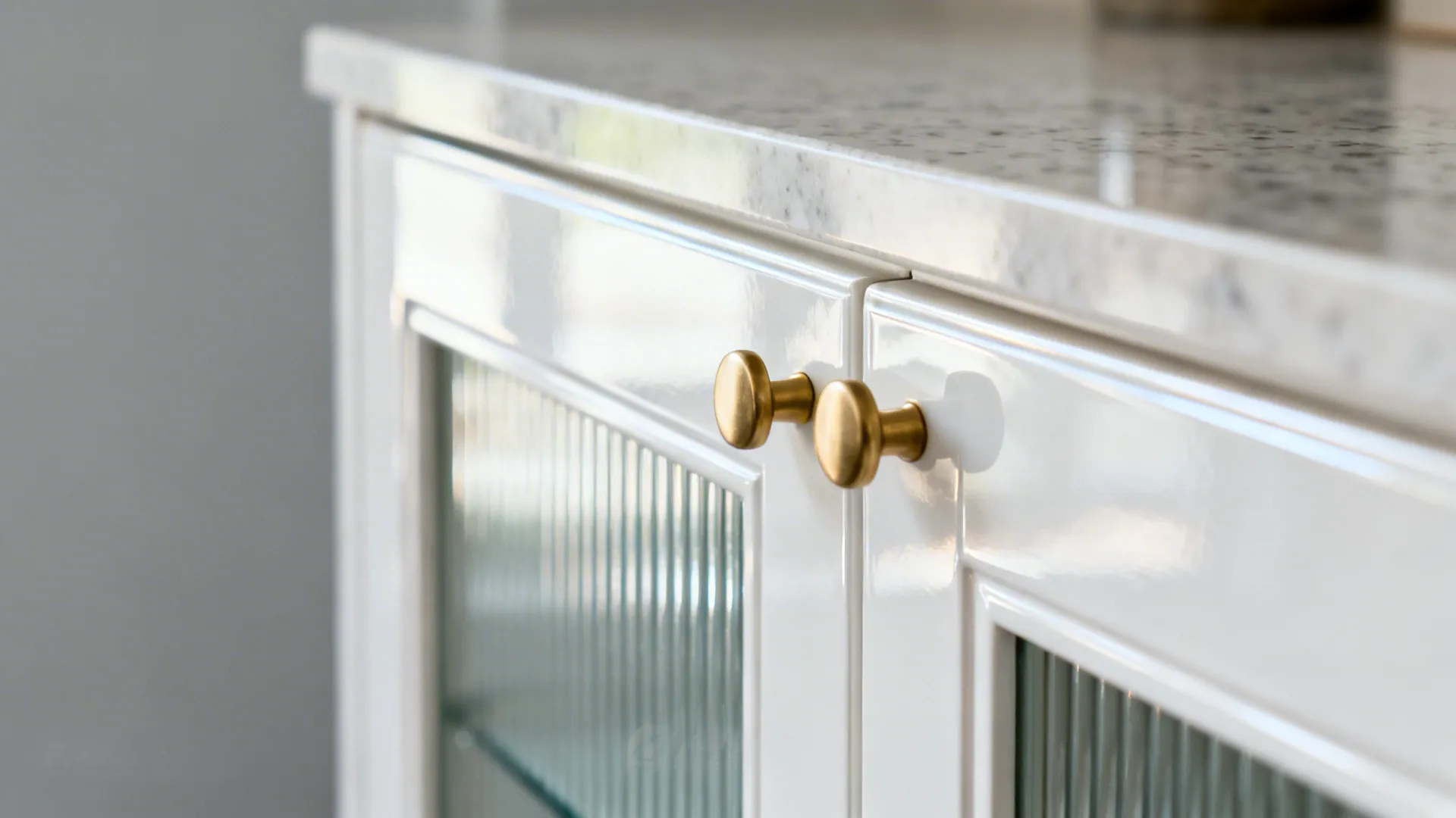 Close up of white kitchen cabinet doors with ribbed glass panels and two gold knobs