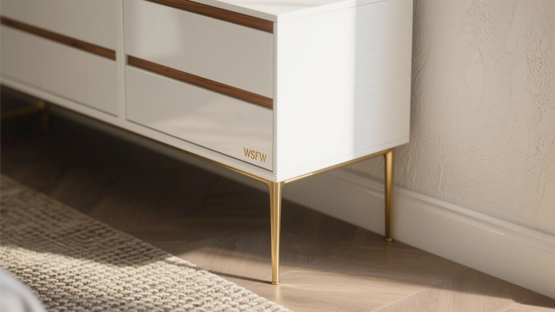 Modern white cabinet with gold metal legs standing on wooden floor near a textured wall