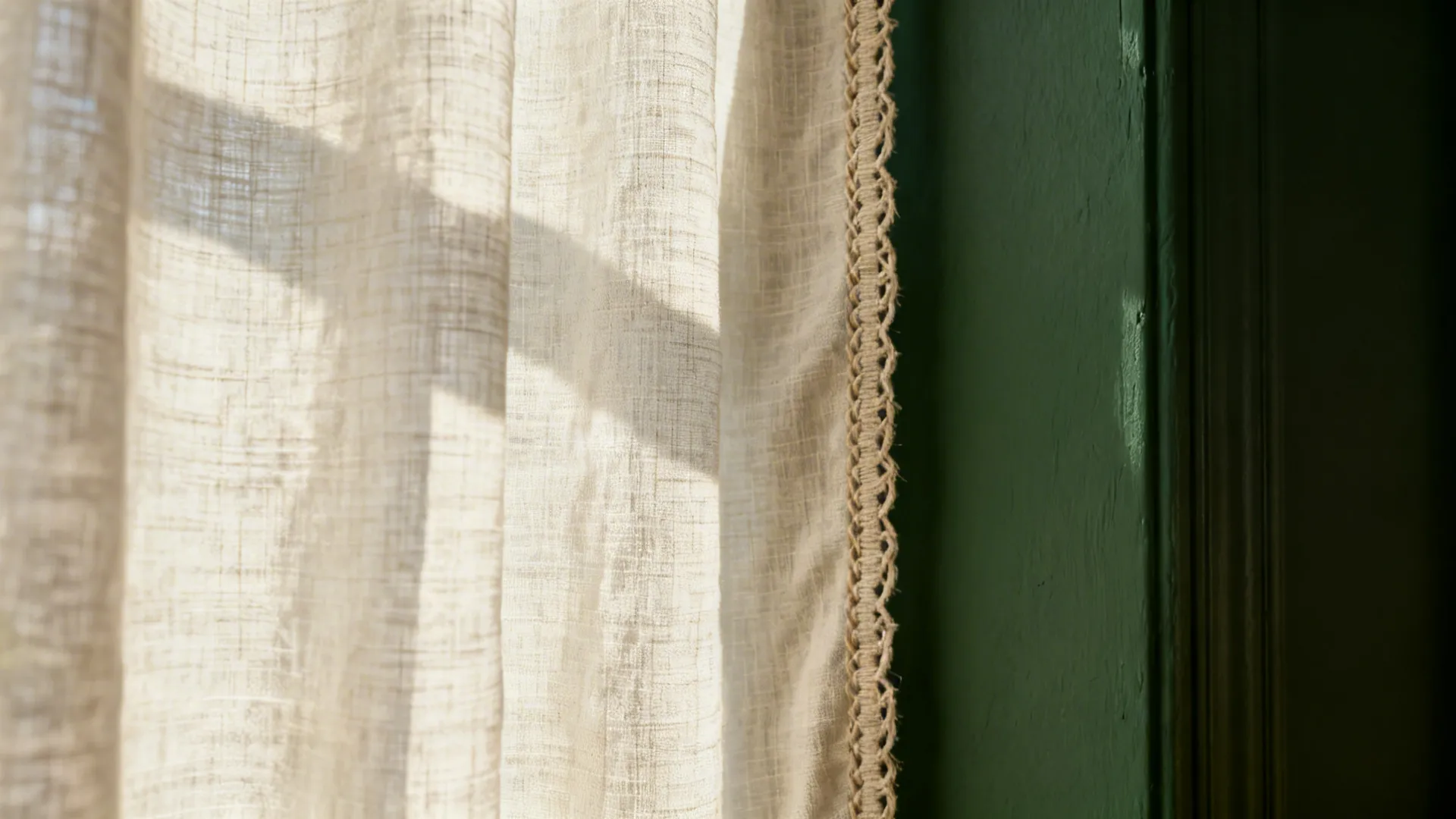 Close up of white linen curtain with lace edge hanging in front of green wall
