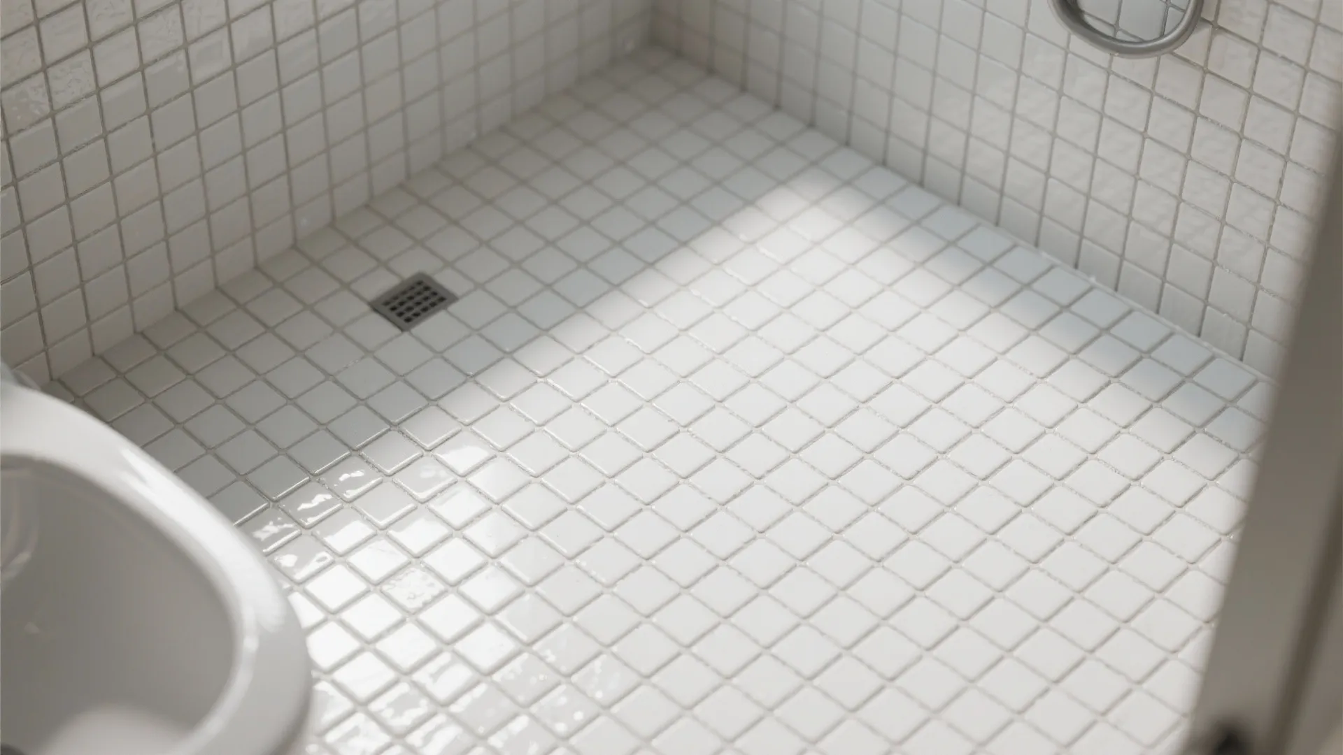 Close up of white square mosaic floor tiles in a bright shower area with drain