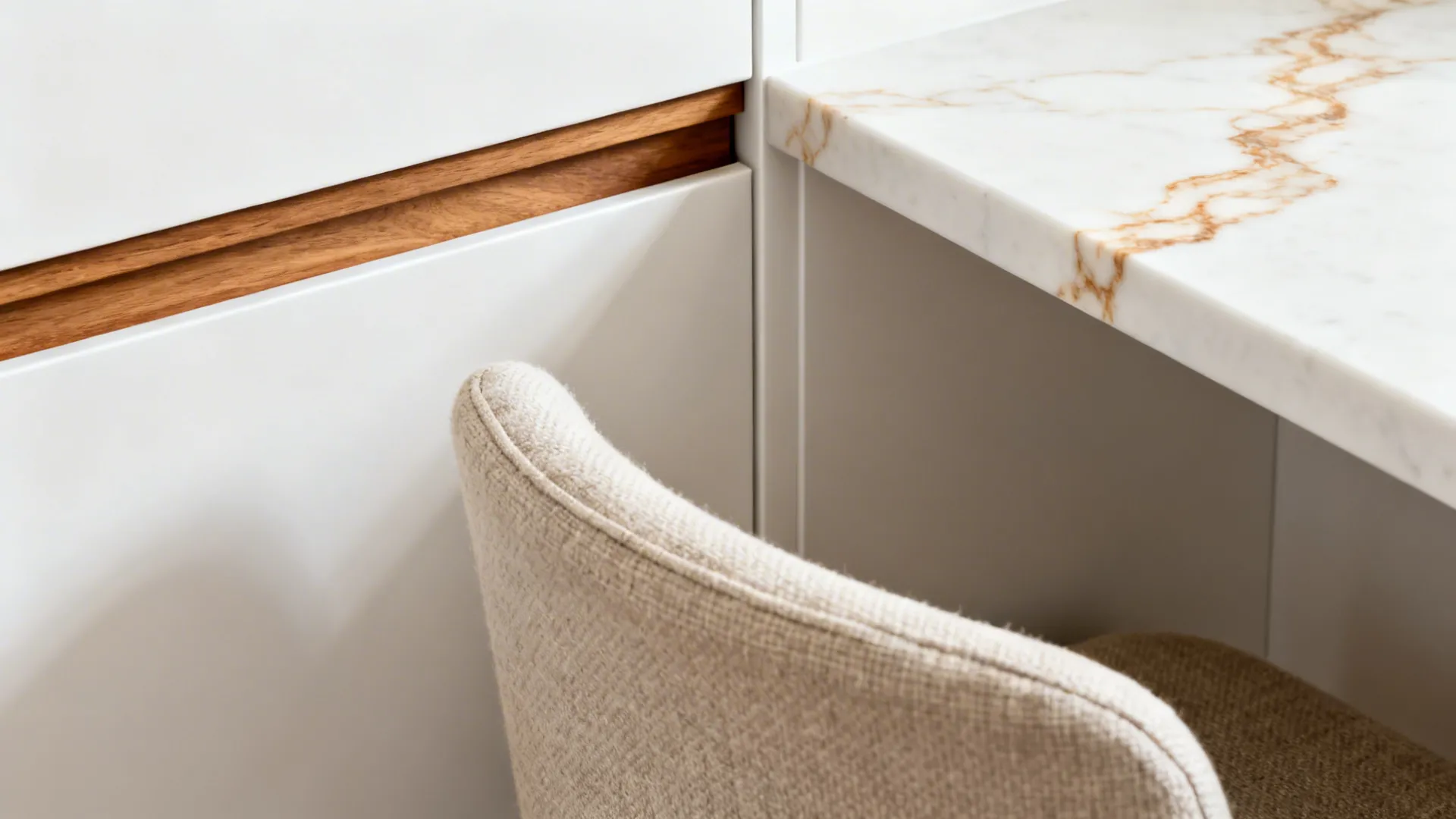 Macro of matte white cabinet, oak trim, and linen-textured stool with veined countertop.
