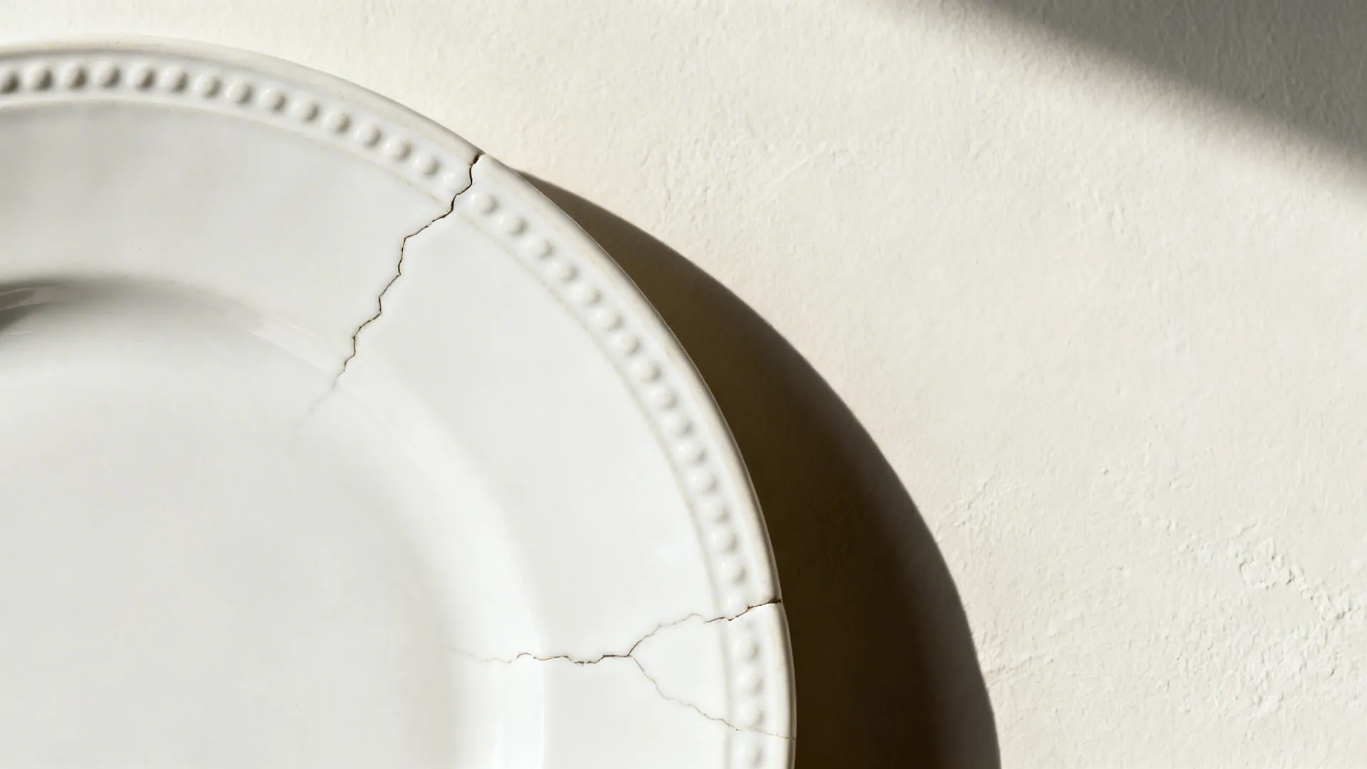 Macro view of a white plate’s embossed rim and subtle glaze texture on a limewash wall.