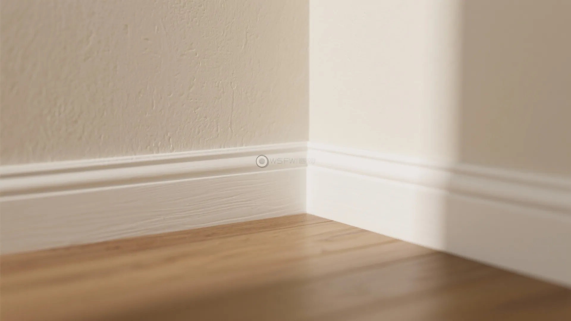 Close up of white floor trim board against a beige wall and light wood flooring corner