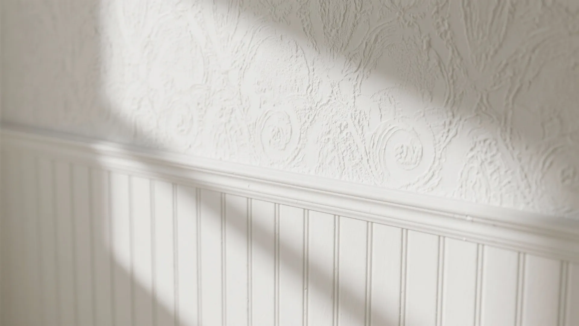 Close up of white wall with patterned wallpaper on top and vertical wall panel below