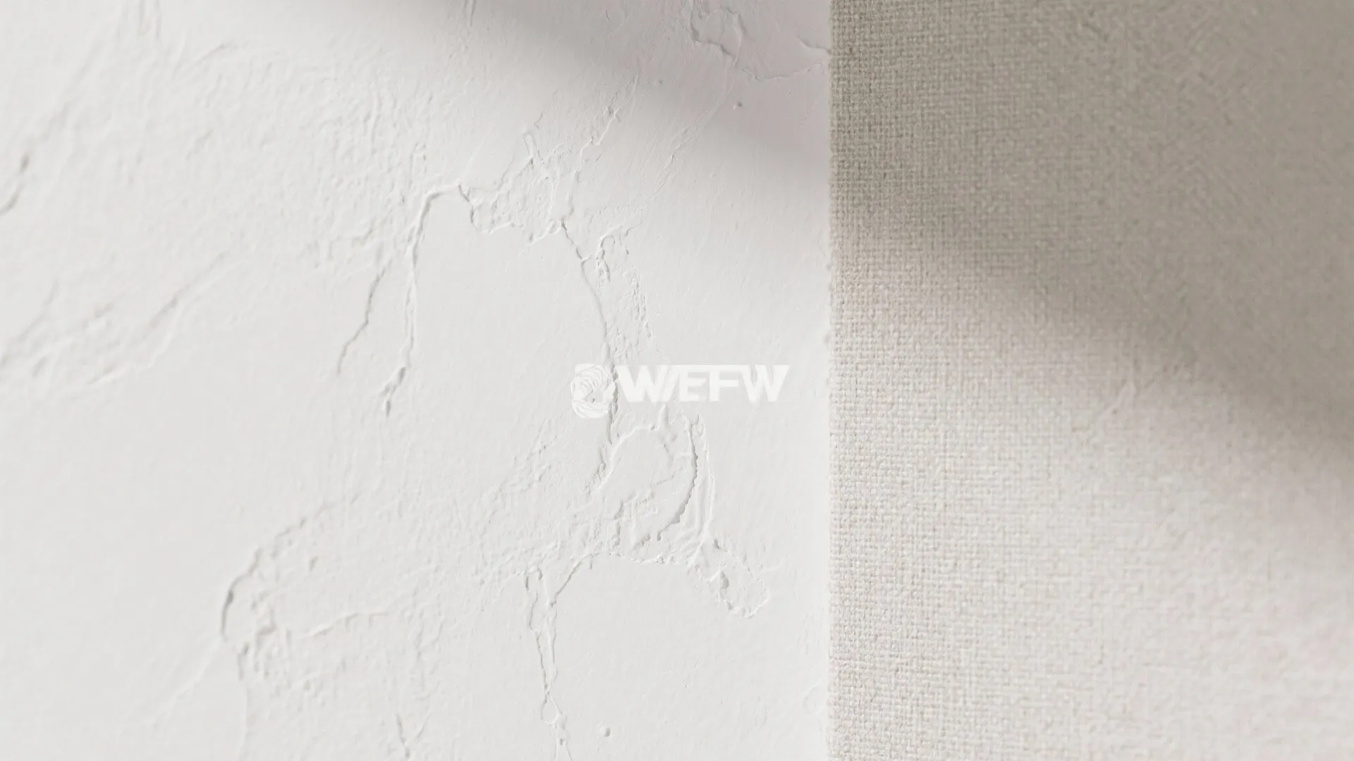 Close-up of white wall texture with uneven plaster surface next to a light beige fabric