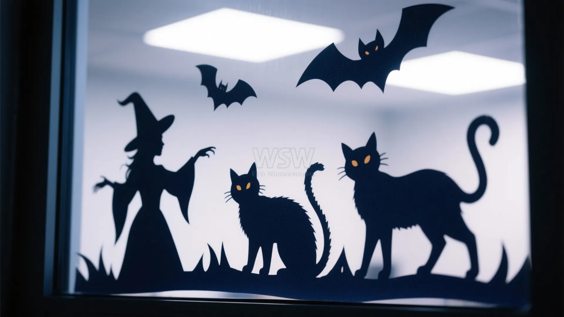 Glass window featuring black Halloween silhouettes of a witch flying bats and two large black cats