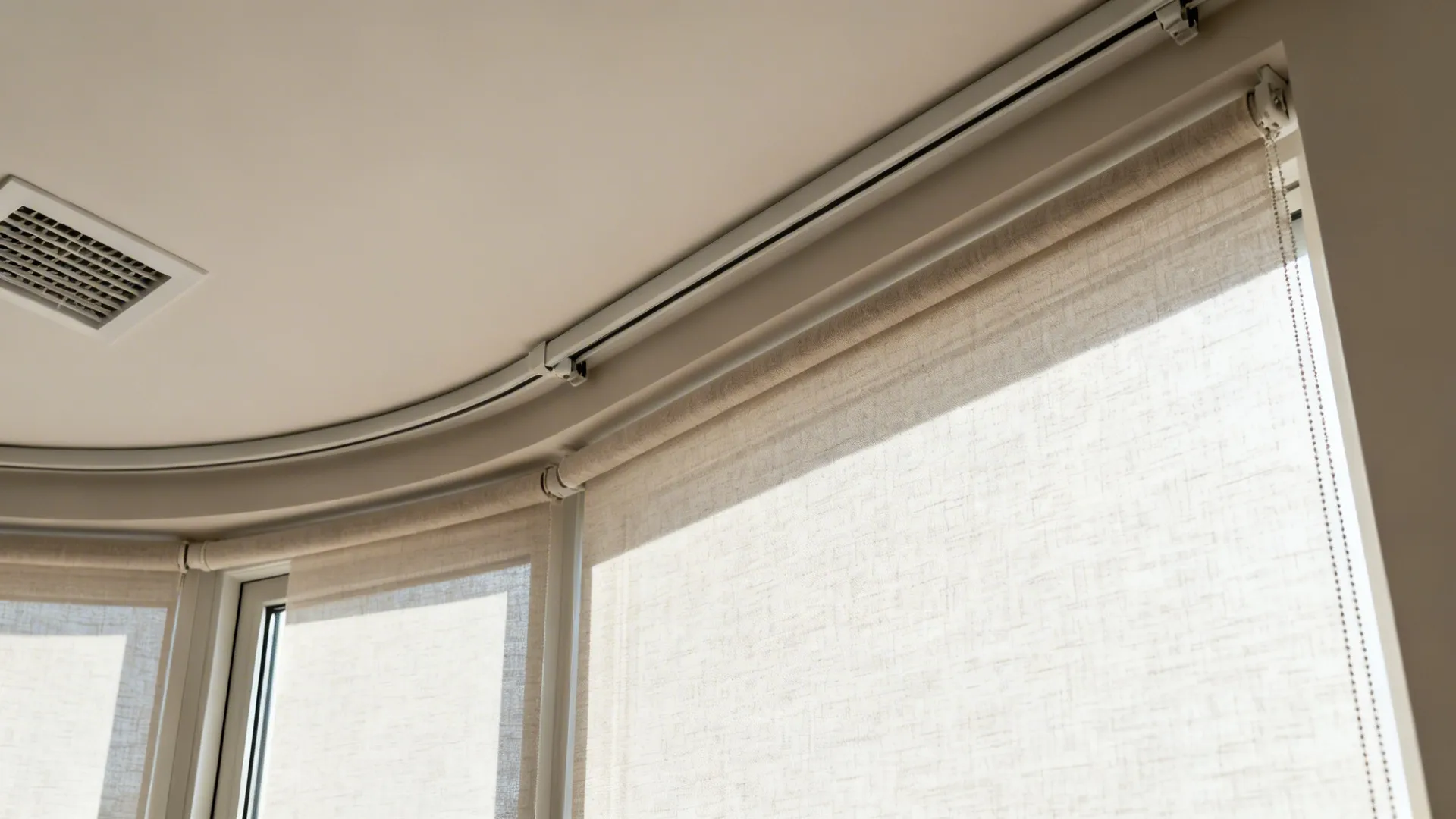 Curved curtain track and light colored roller blinds installed on the top of a window